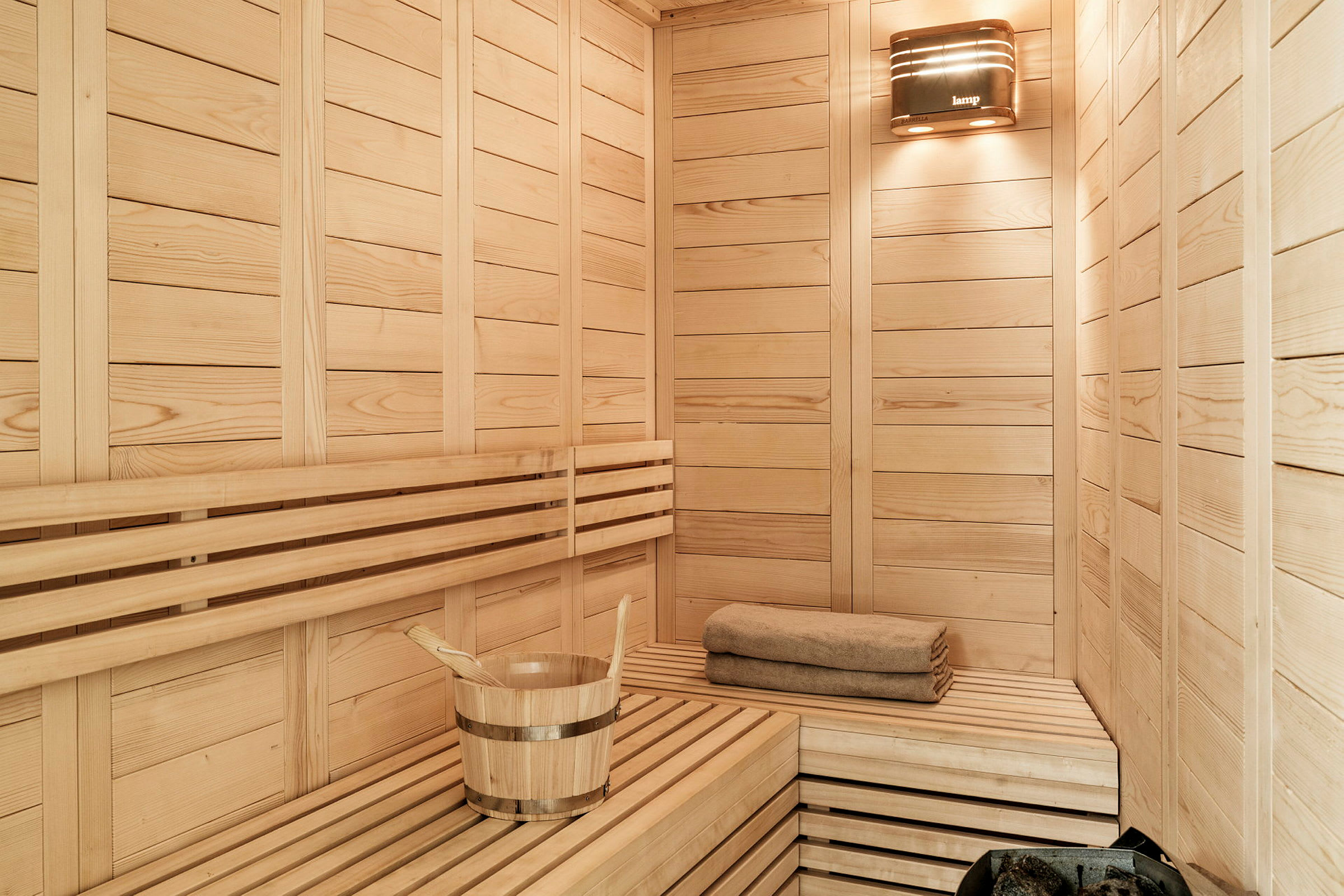 Sauna, jossa on puupaneelit, puinen ämpäri kauhalla ja taiteltu pyyhe. (Tekoälyn luoma teksti)