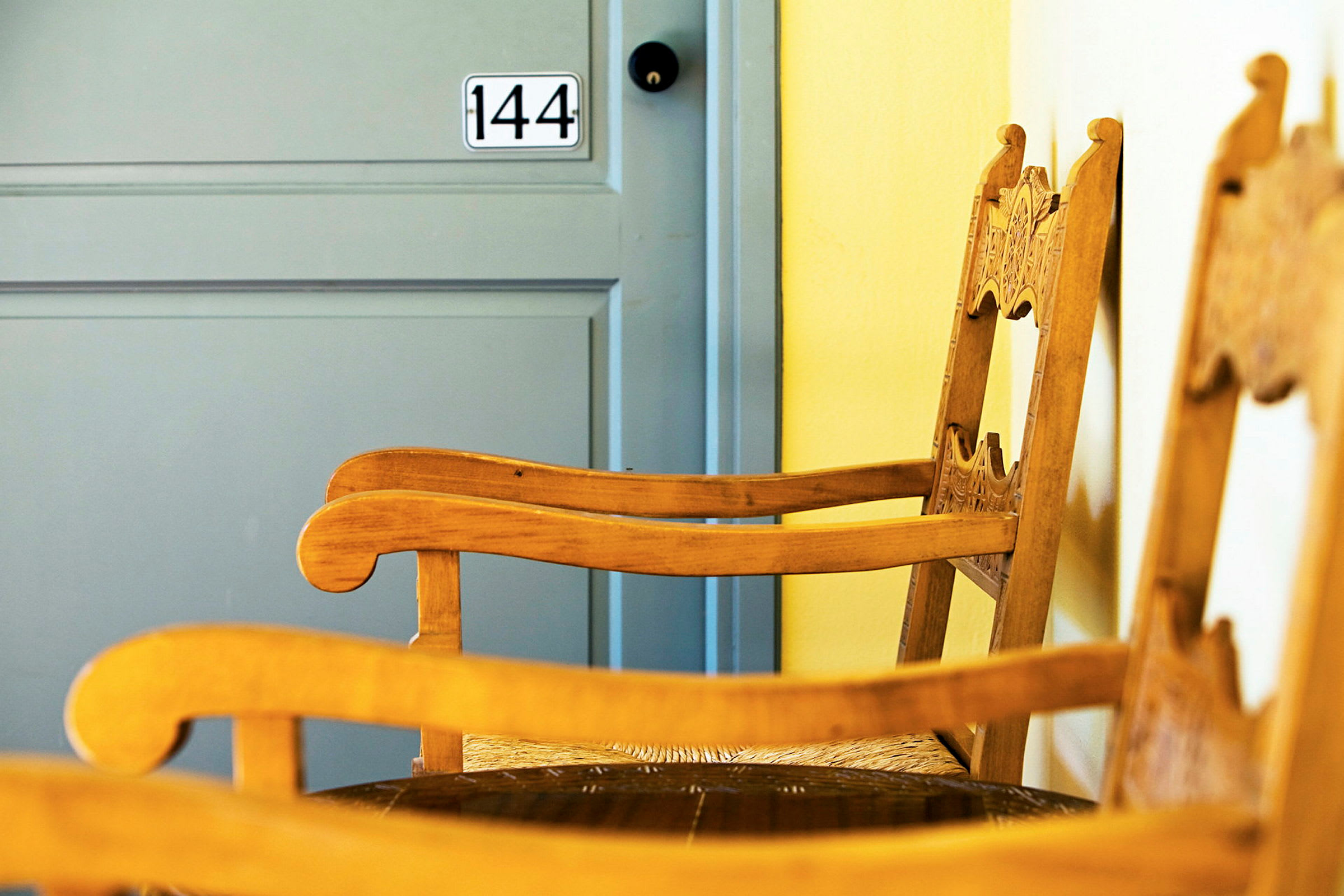 Kaksi koristeellisilla selkänojilla varustettua puutuolia sijoitettuna sinisen oven eteen, jossa numero 144. (Tekoälyn luoma teksti)