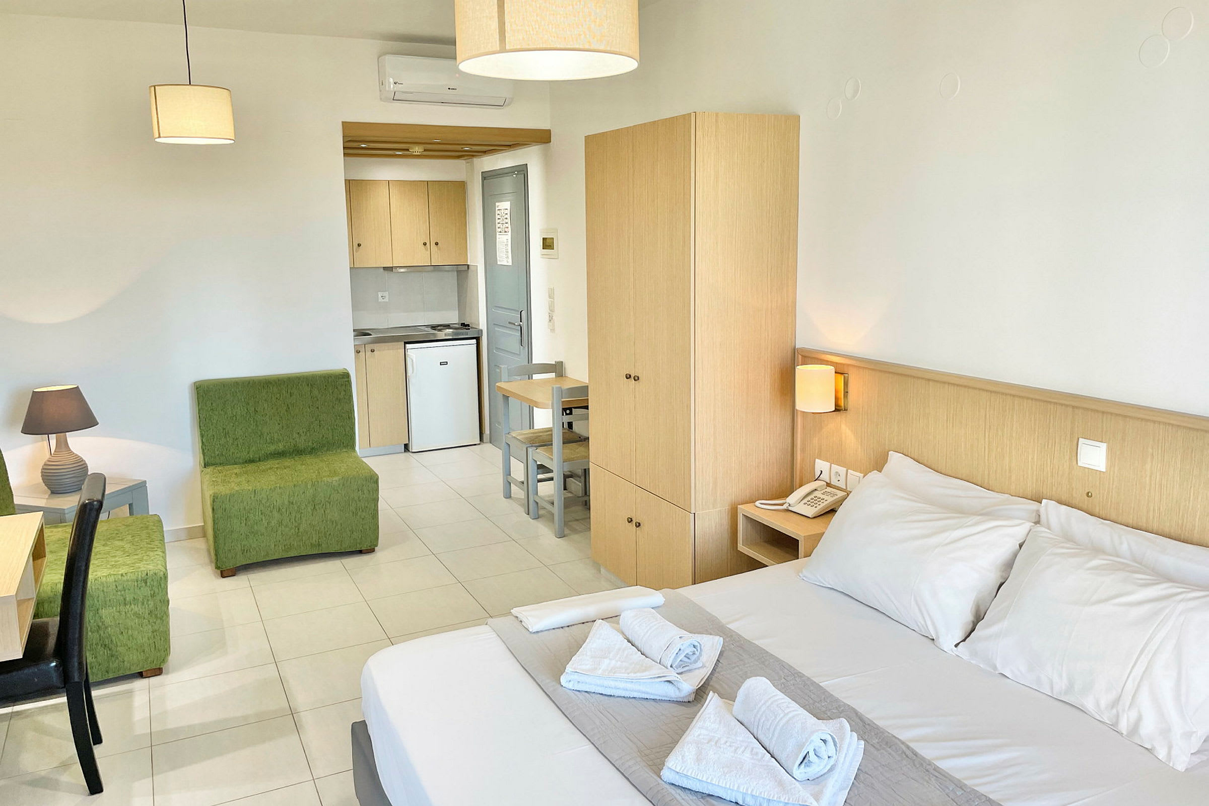 Hotellihuone, jossa on parivuode, vihreä istuinryhmä, työpöytä, vaatekaappi ja keittokomero. (Tekoälyn luoma teksti)