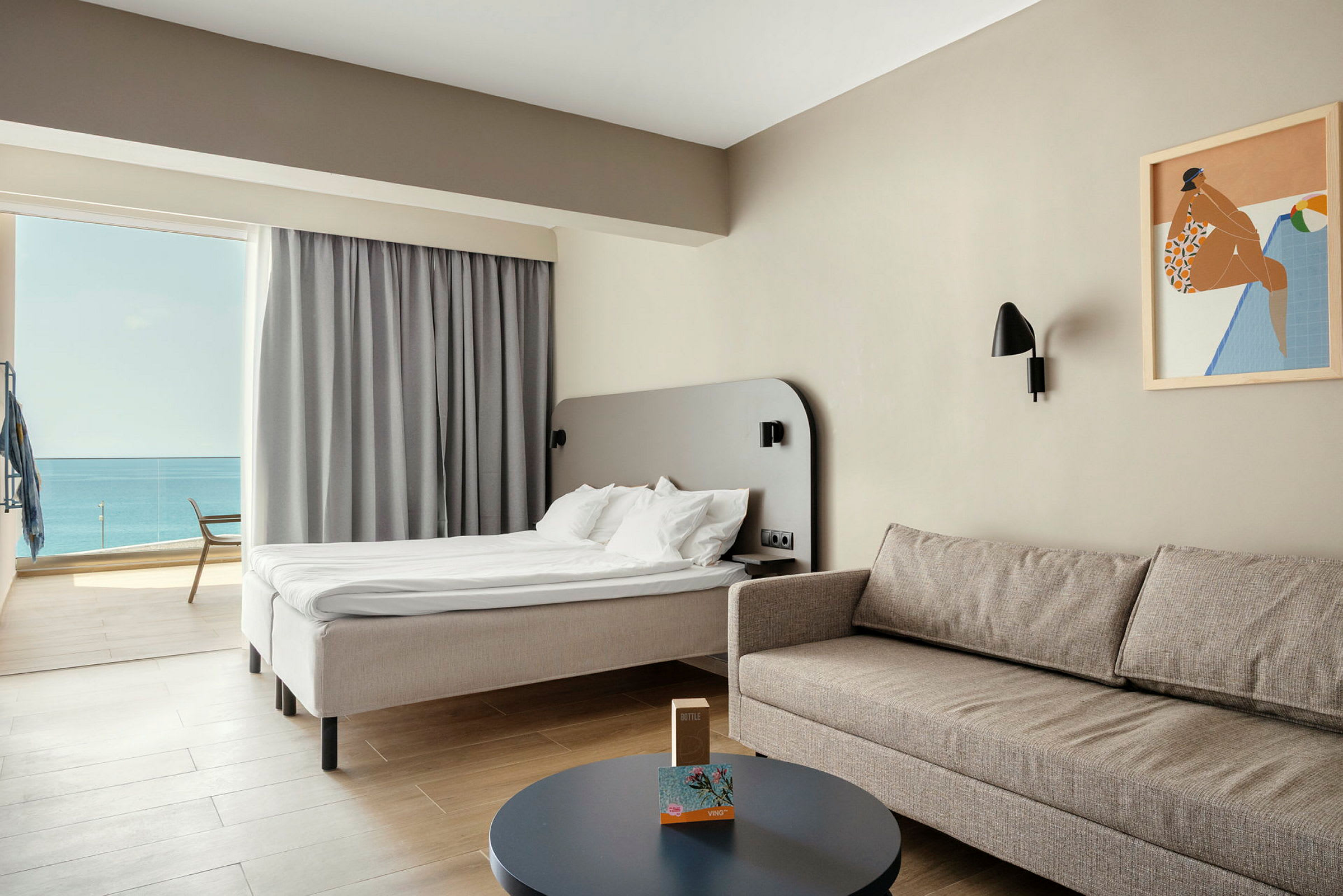 Deluxe-hotellihuone, jossa on vaalea sisustus, mukava sohva, pöytä ja sänky, jolta on näköala merelle. (Tekoälyn luoma teksti)