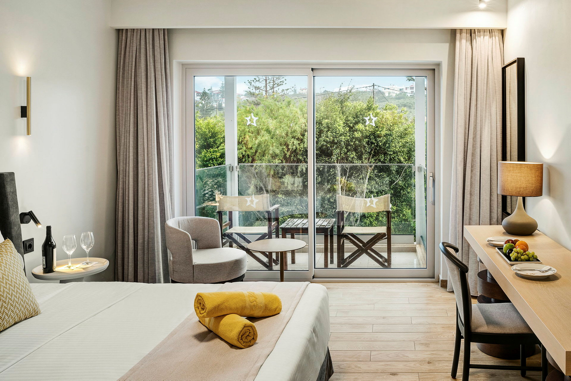 Hotellihuone, jossa on vuode, kirjoituspöytä ja parveke näköalalla vehreyteen. (Tekoälyn luoma teksti)