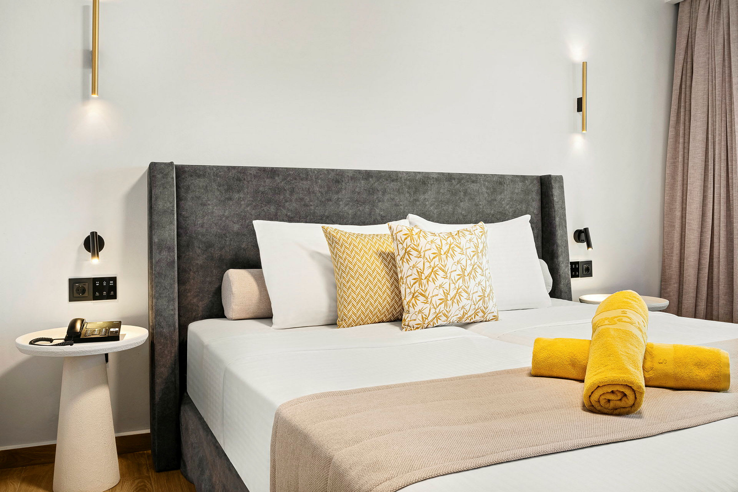 Hotellihuone, jossa on suuri sänky, koristeltu tyynyillä ja rullatuilla pyyhkeillä peiton päällä. Pöytä, jossa on puhelin, näkyy sängyn vieressä. (Tekoälyn luoma teksti)