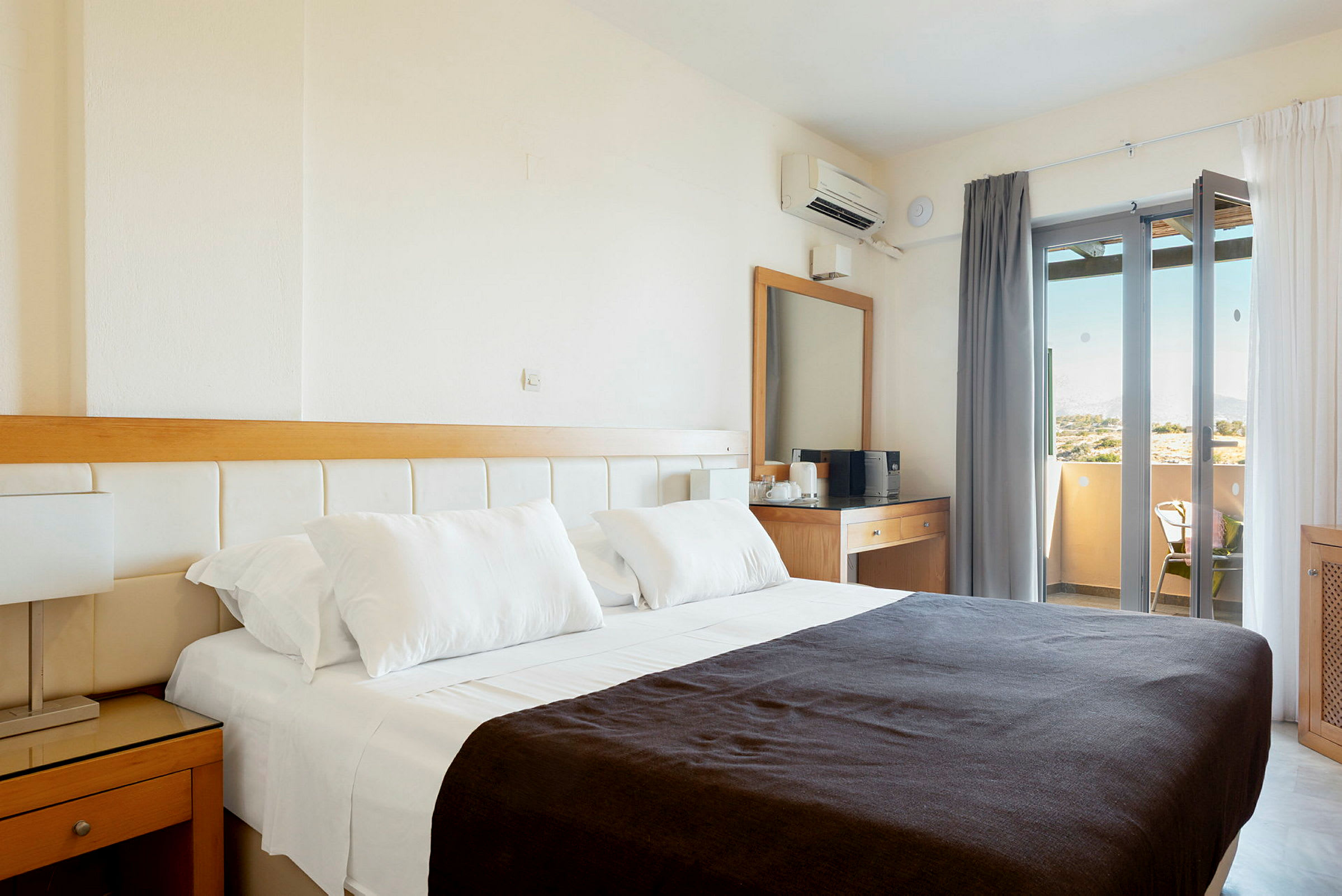 Hotellihuone, jossa on parivuode, valkoiset lakanat ja tumma peitto. Huoneessa on myös kirjoituspöytä peilillä ja parveke näkymällä. (Tekoälyn luoma teksti)