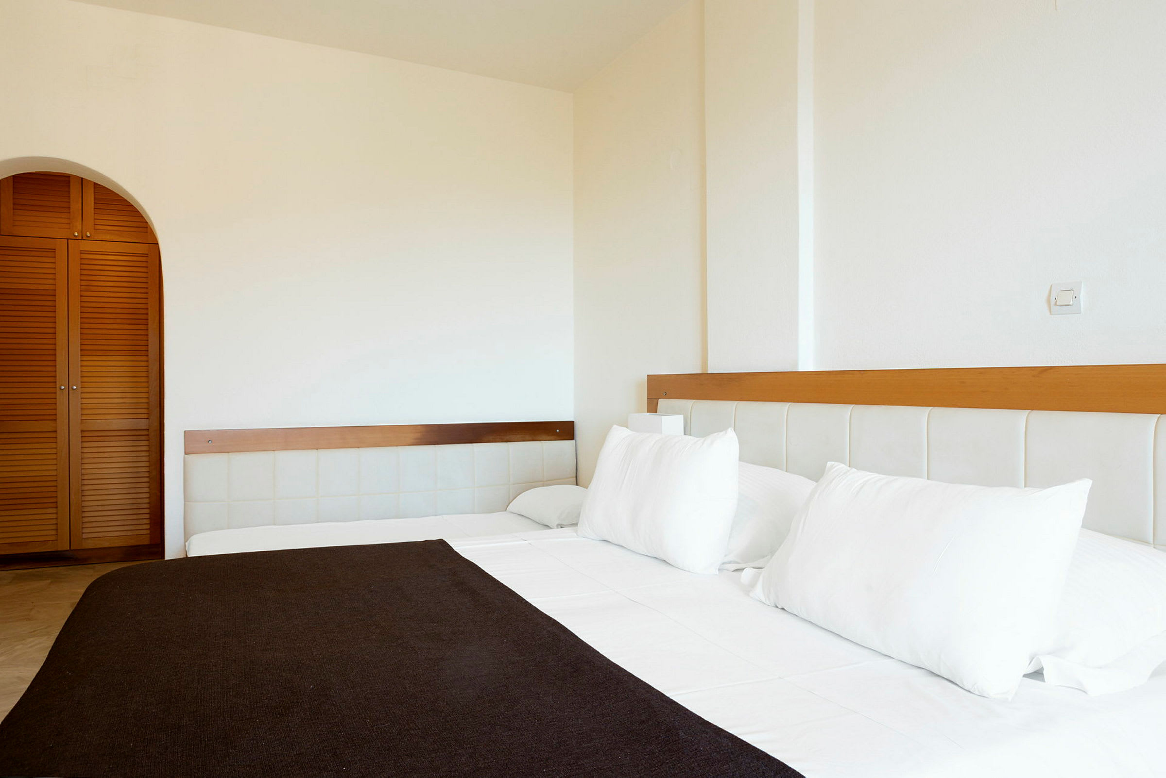 Hotellihuone, jossa on vuode pedattuna valkoisilla lakanoilla ja tyynyillä. Taustalla näkyy vaatekaappi puuovilla. (Tekoälyn luoma teksti)