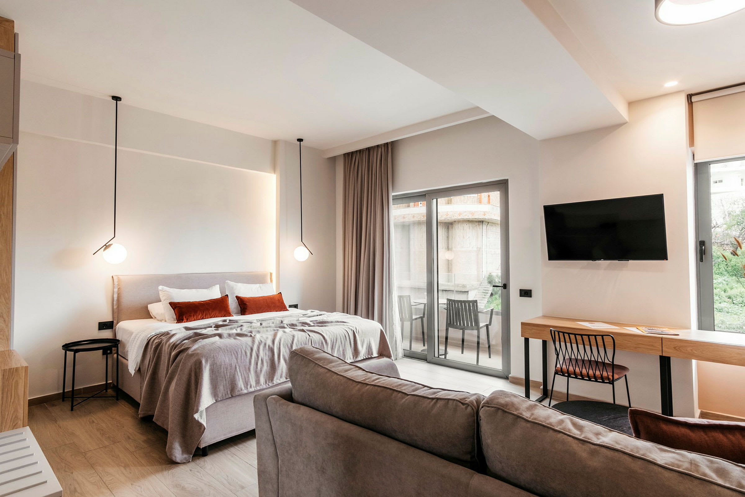 Nykyaikainen hotellihuone, jossa on sänky, sohva, kirjoituspöytä, televisio ja parveke. (Tekoälyn luoma teksti)