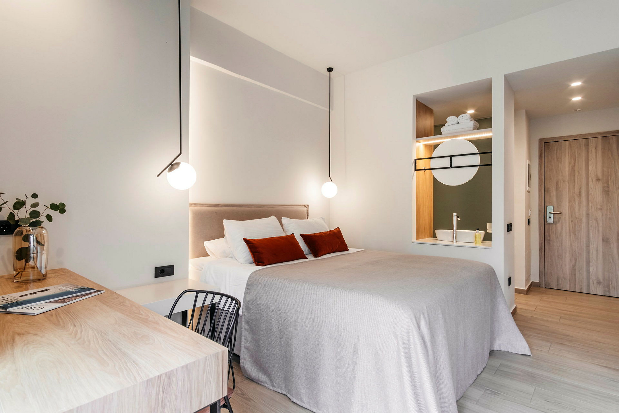 Nykyaikaisesti sisustettu hotellihuone, jossa parivuode, työpöytä ja integroitu pesuallas peileineen. (Tekoälyn luoma teksti)
