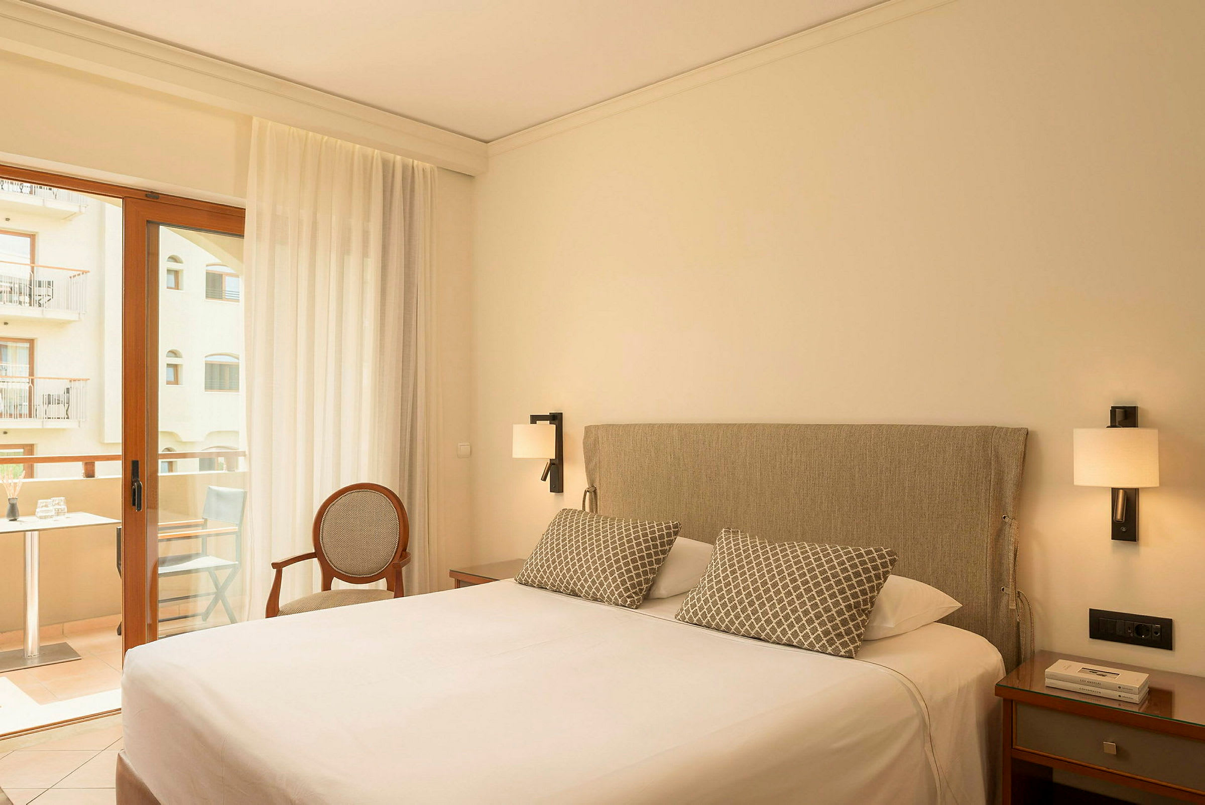 Hotellihuone, jossa on parivuode, yöpöydät, tuoli ja parvekeovi näkymällä parvekkeelle. (Tekoälyn luoma teksti)