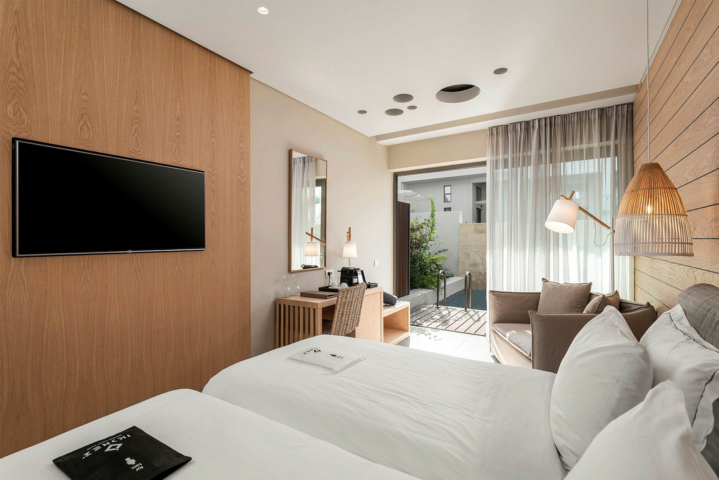 Hotellihuone, jossa kaksi sänkyä, työpöytä ja oleskelutila. Ovi, joka johtaa pienelle uima-altaalle. (Tekoälyn luoma teksti)