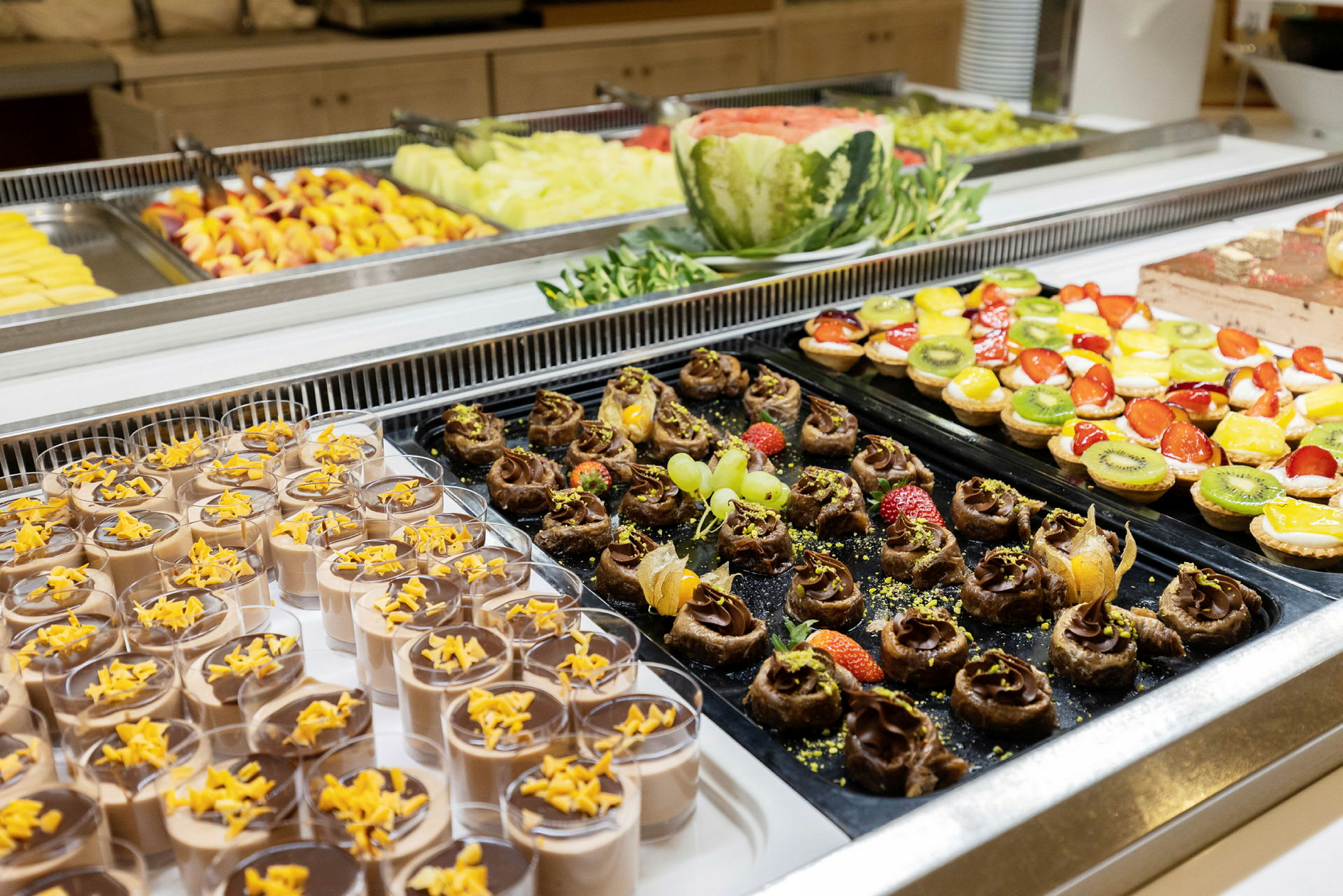 Buffet, jossa erilaisia jälkiruokia, mukaan lukien suklaamoussea, hedelmäkoristeita ja pieniä kakkuja. (Tekoälyn luoma teksti)