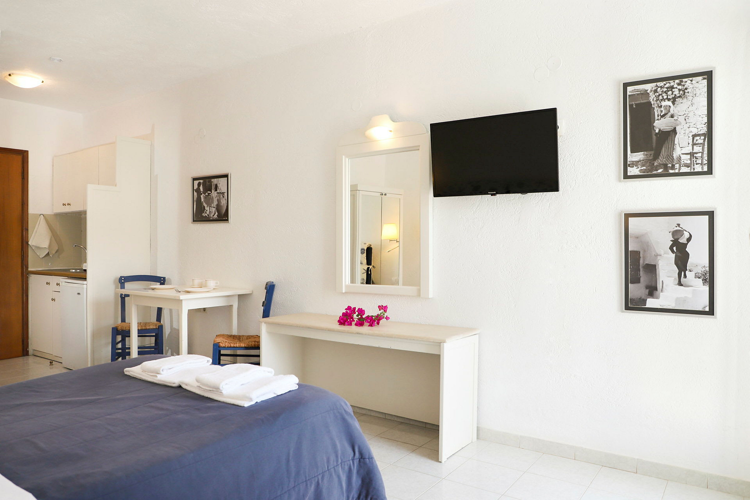Hotellihuone, jossa on parisänky, valkoisia huonekaluja, seinälle kiinnitetty televisio ja mustavalkoiset taulut seinällä. (Tekoälyn luoma teksti)