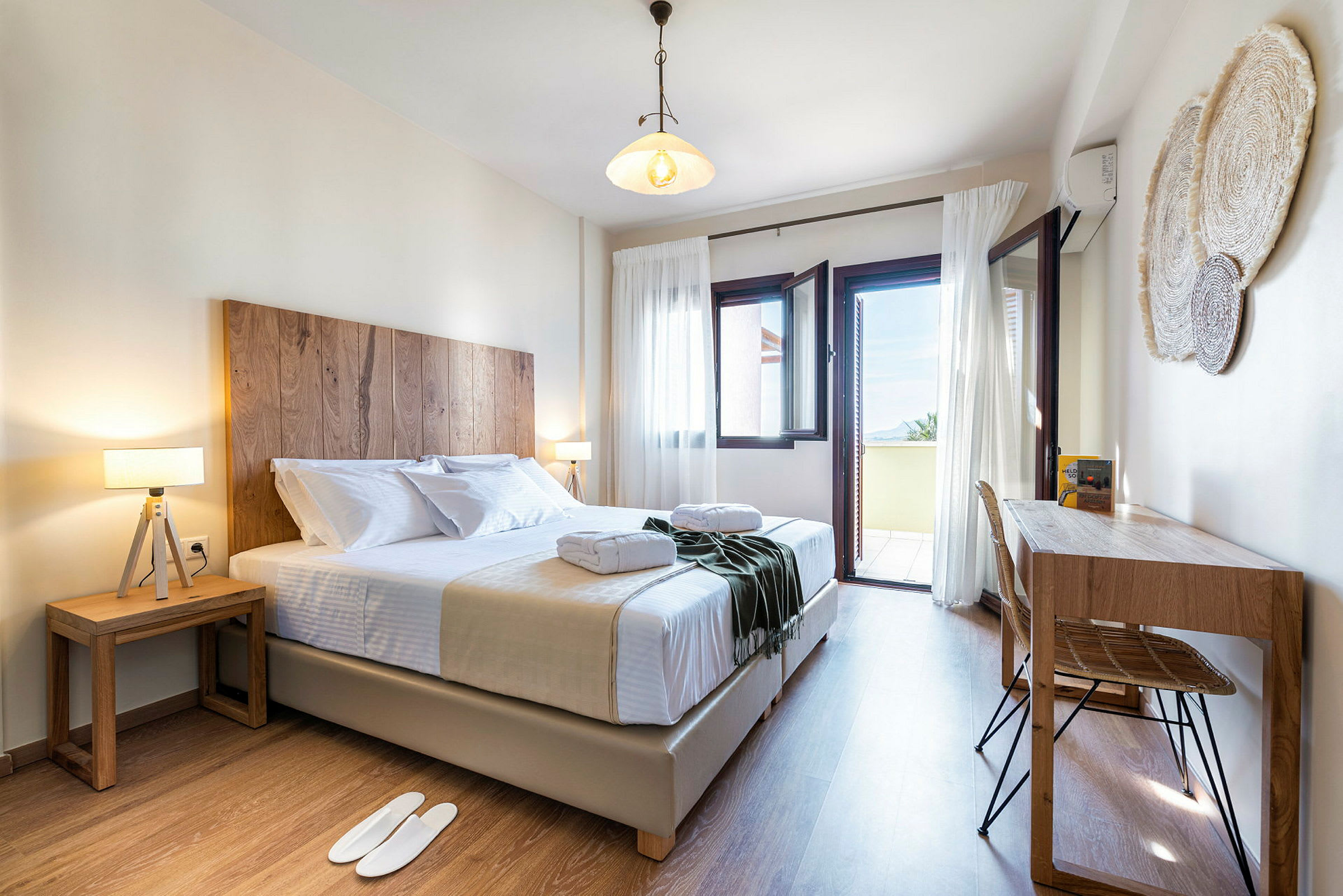 Valoisa ja kutsuva hotellihuone, jossa on parivuode, kaksi yöpöytää ja kirjoituspöytä. Ikkunat ovat avoinna parvekkeelle, josta on näkymä. (Tekoälyn luoma teksti)