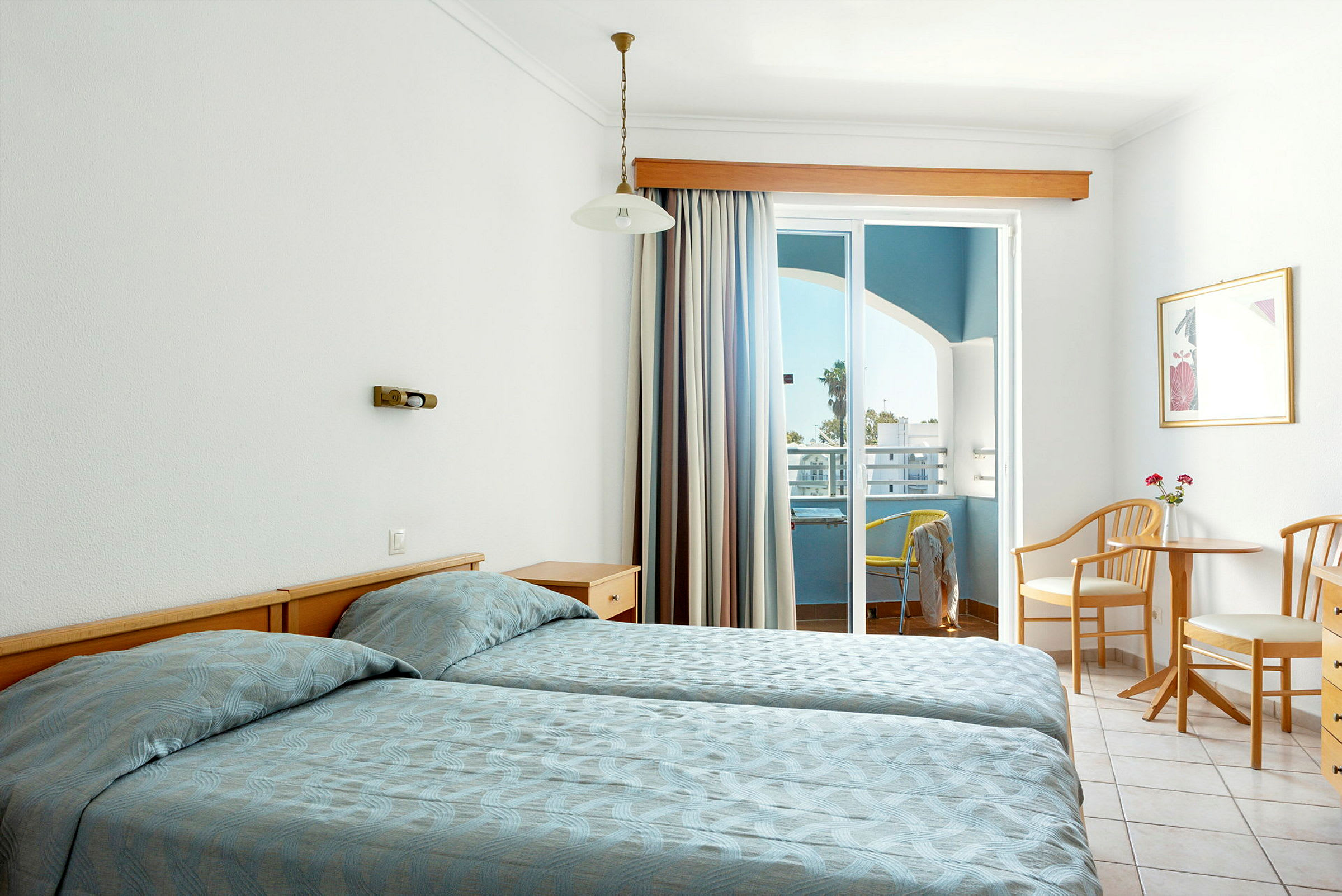Hotellihuone, jossa on kaksi yhden hengen sänkyä, pöytä ja kaksi tuolia sekä parveke näkymällä. (Tekoälyn luoma teksti)