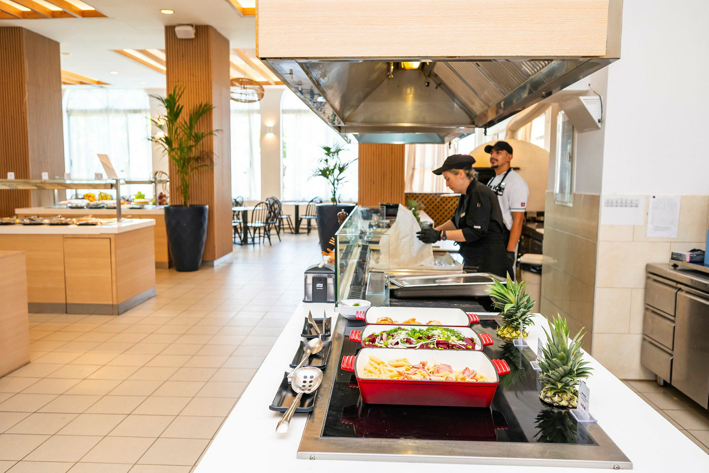 Buffetalue, jossa ruoka on aseteltu värikkäisiin tarjoiluastioihin ja keittiöhenkilökunta työpisteellä. (Tekoälyn luoma teksti)