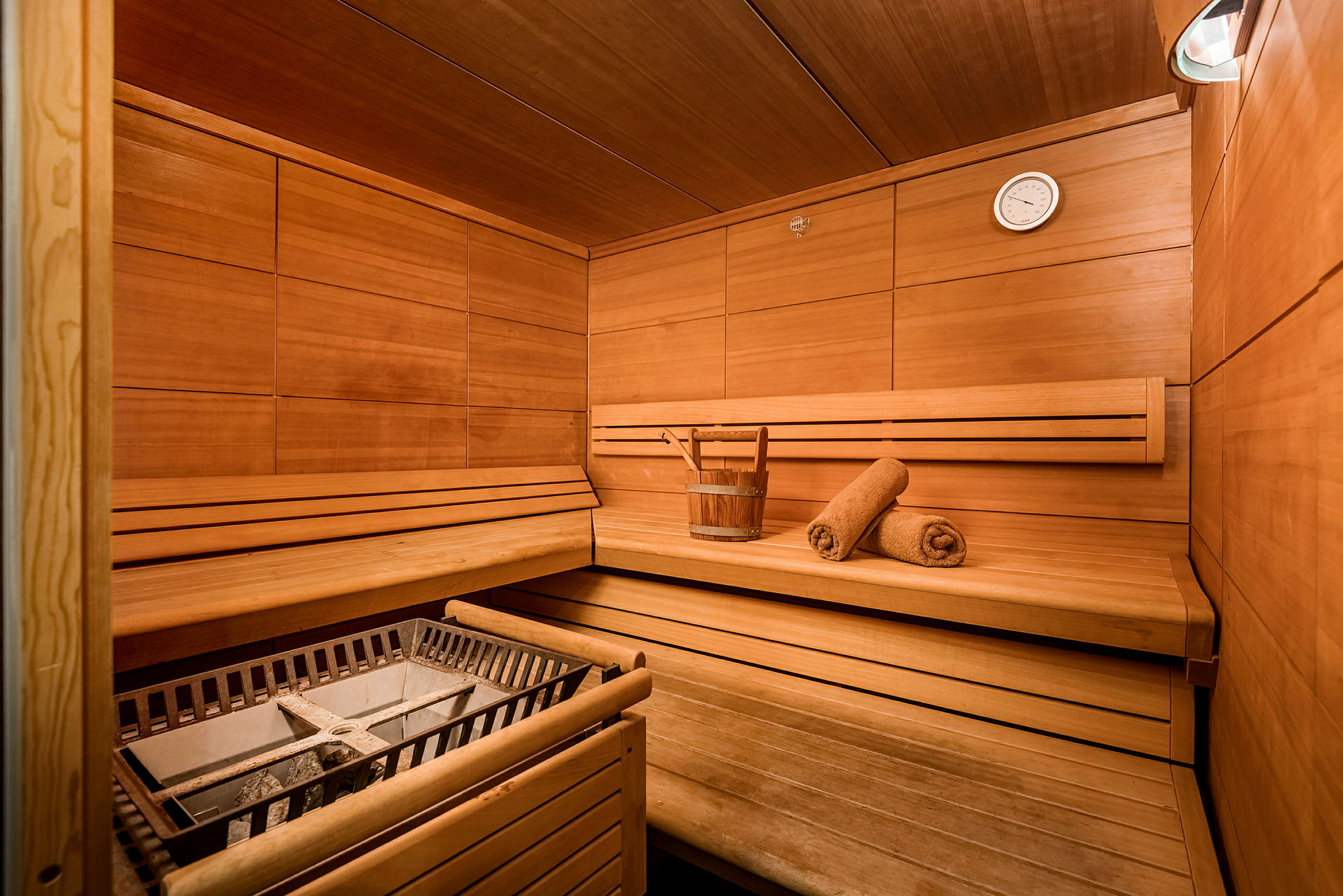 Puuvuorattu sauna, jossa istuimia, ämpäri ja kaksi pyyhettä. (Tekoälyn luoma teksti)
