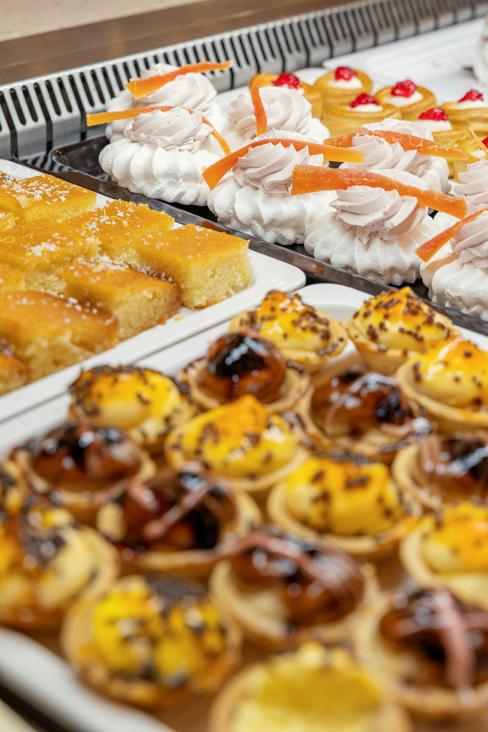 Leivonnaisten buffet, jossa on pieniä kakkuja kermavaahdolla, kakkupaloja ja pieniä piirakoita. (Tekoälyn luoma teksti)