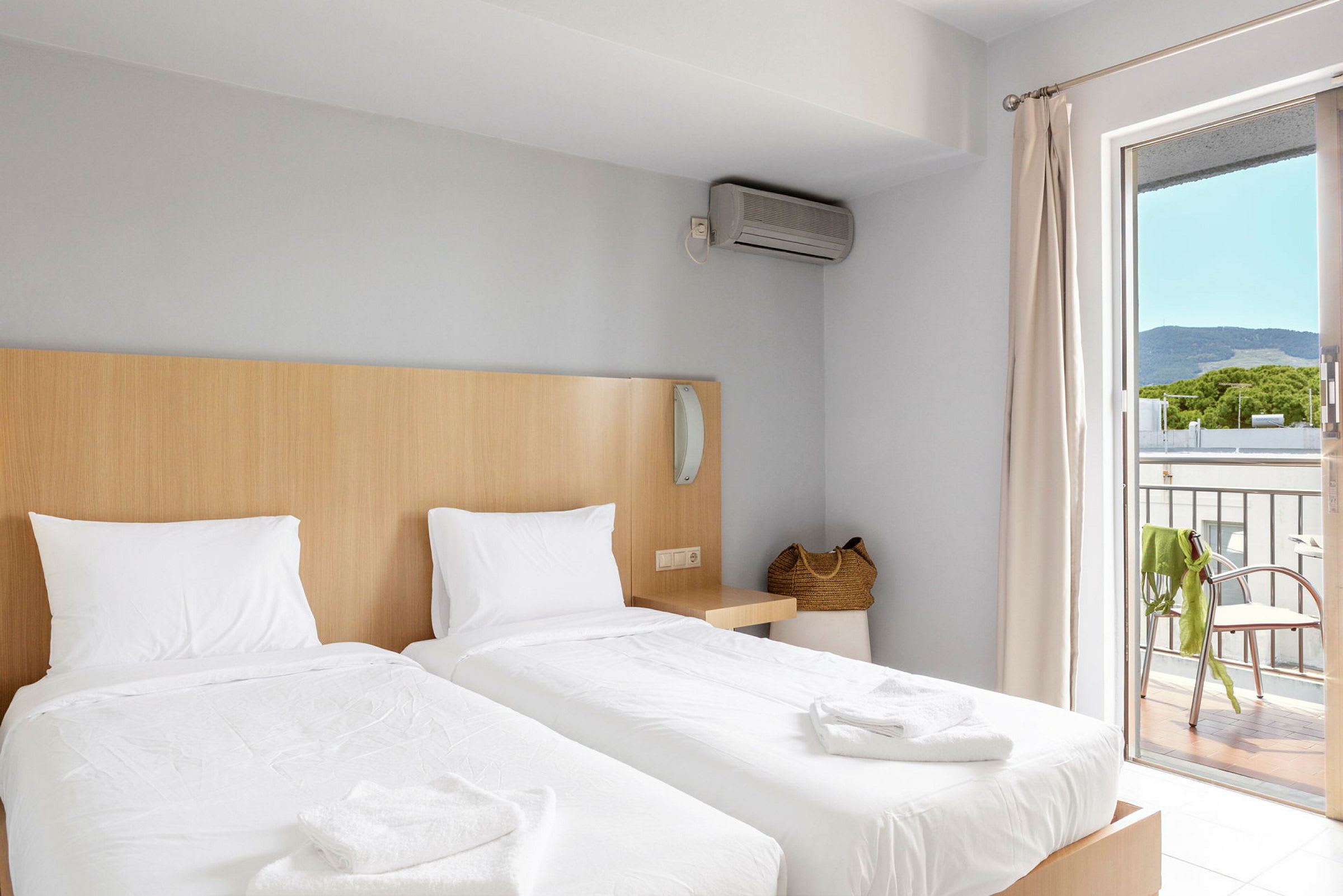 Hotellihuone, jossa on kaksi erillistä vuodetta, korilaukku ja parveke näkymillä. (Tekoälyn luoma teksti)