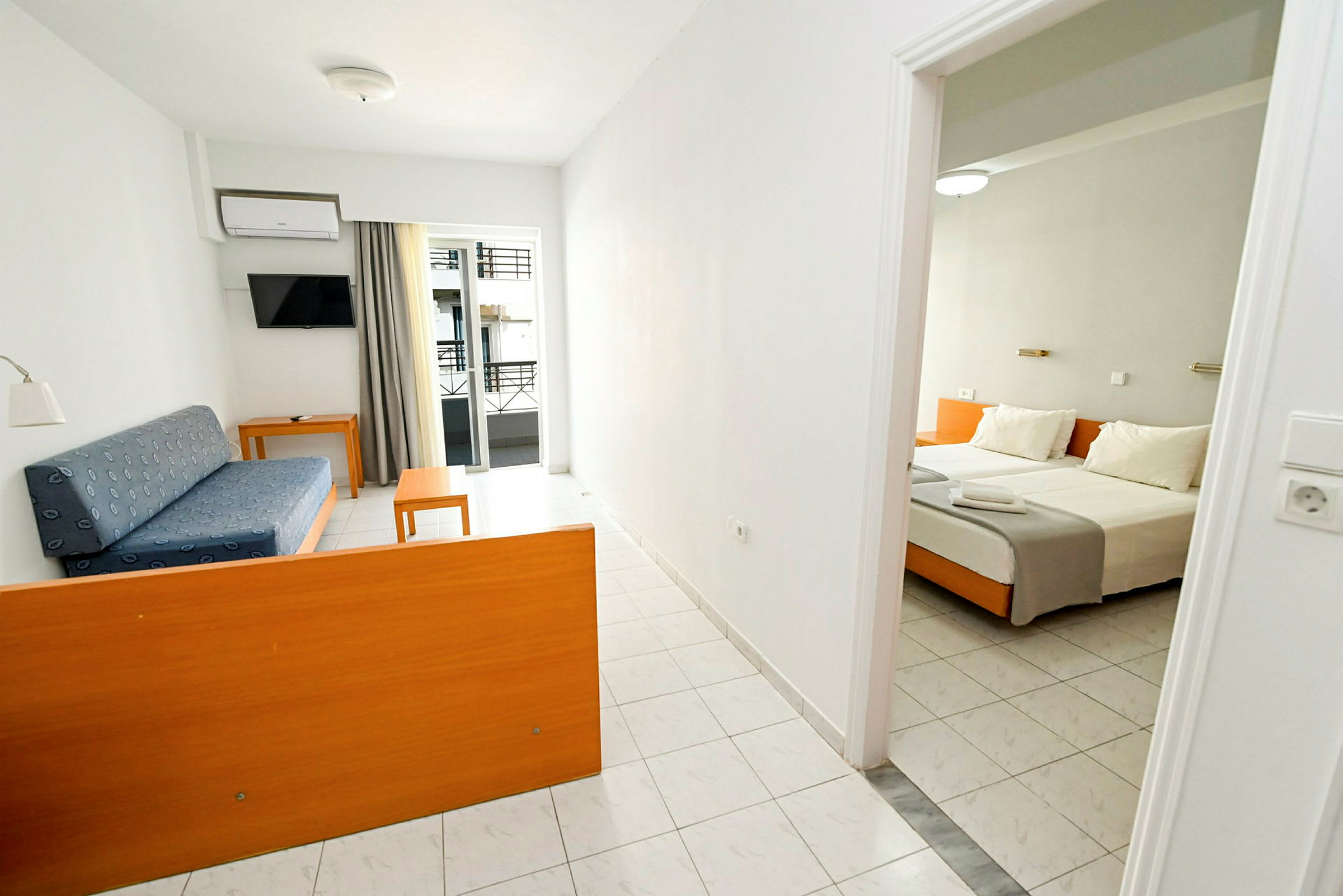 Hotellihuone, jossa oleskelutila sinisellä sohvalla ja pöydällä sekä makuutila parivuoteella. (Tekoälyn luoma teksti)