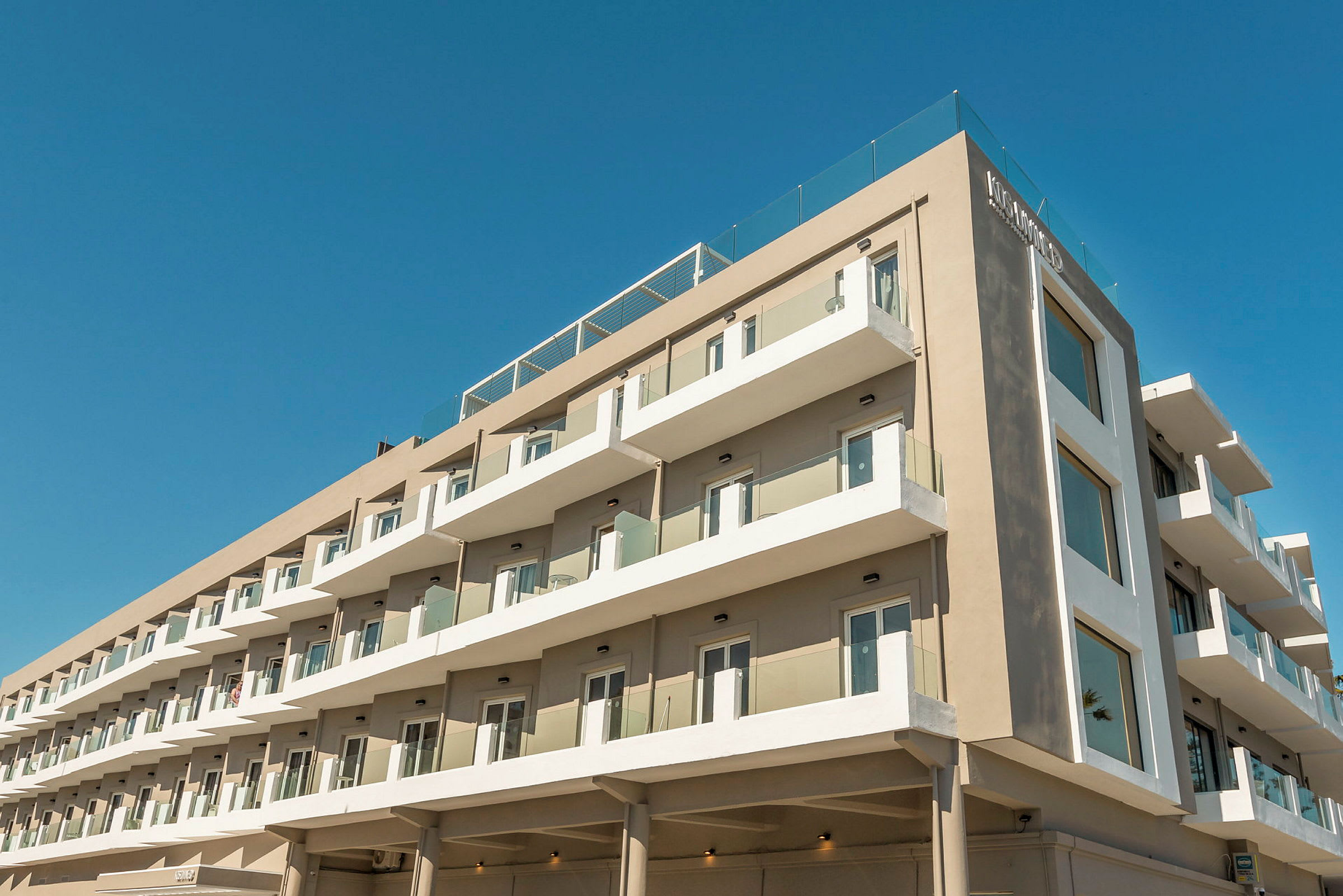 Nykyaikainen hotellirakennus, jossa on useita kerroksia ja parvekkeita sinisen taivaan alla. (Tekoälyn luoma teksti)