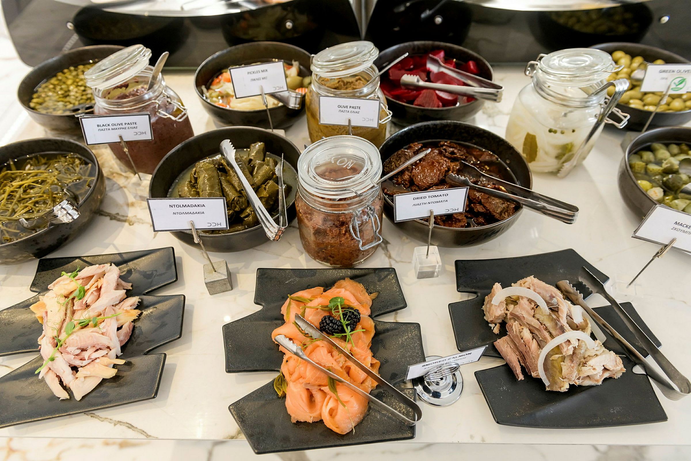 Buffet, jossa on erilaisia alkupaloja ja pikkuruokia, mukaan lukien säilöttyjä ruokia ja kylmiä leikkeitä lautasilla. (Tekoälyn luoma teksti)