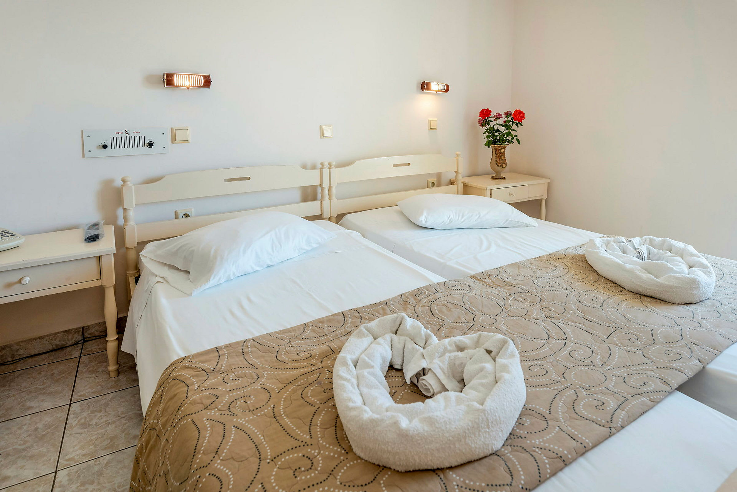 Hotellihuone, jossa on kaksi yhden hengen vuodetta, koriste-esineitä ja kukkavaasi yöpöydällä. (Tekoälyn luoma teksti)