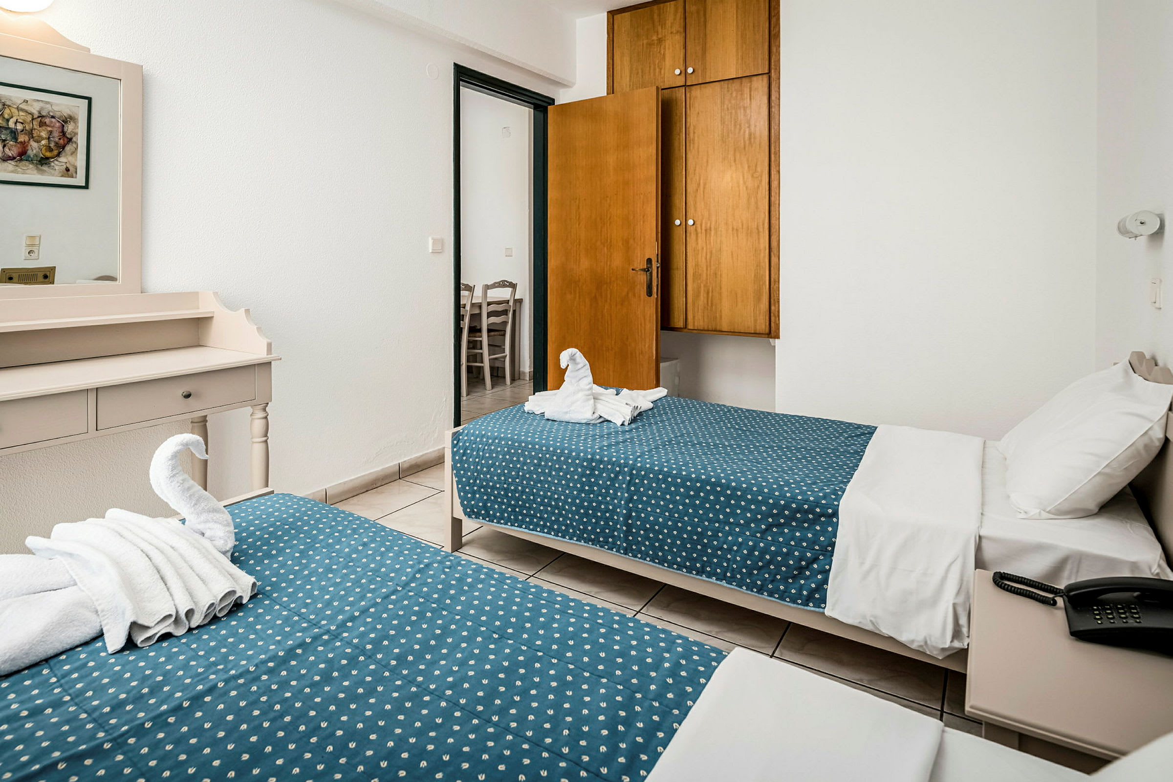 Hotellihuone, jossa on kaksi yhden hengen vuodetta, sininen pilkullinen vuodevaatteet ja puinen lipasto. (Tekoälyn luoma teksti)