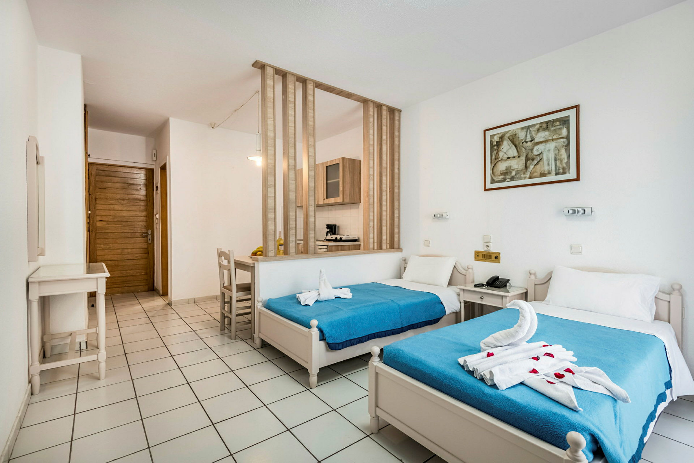 Hotellihuone, jossa on kaksi yhden hengen sänkyä, siniset päiväpeitteet ja koristellut pyyhkeet. (Tekoälyn luoma teksti)