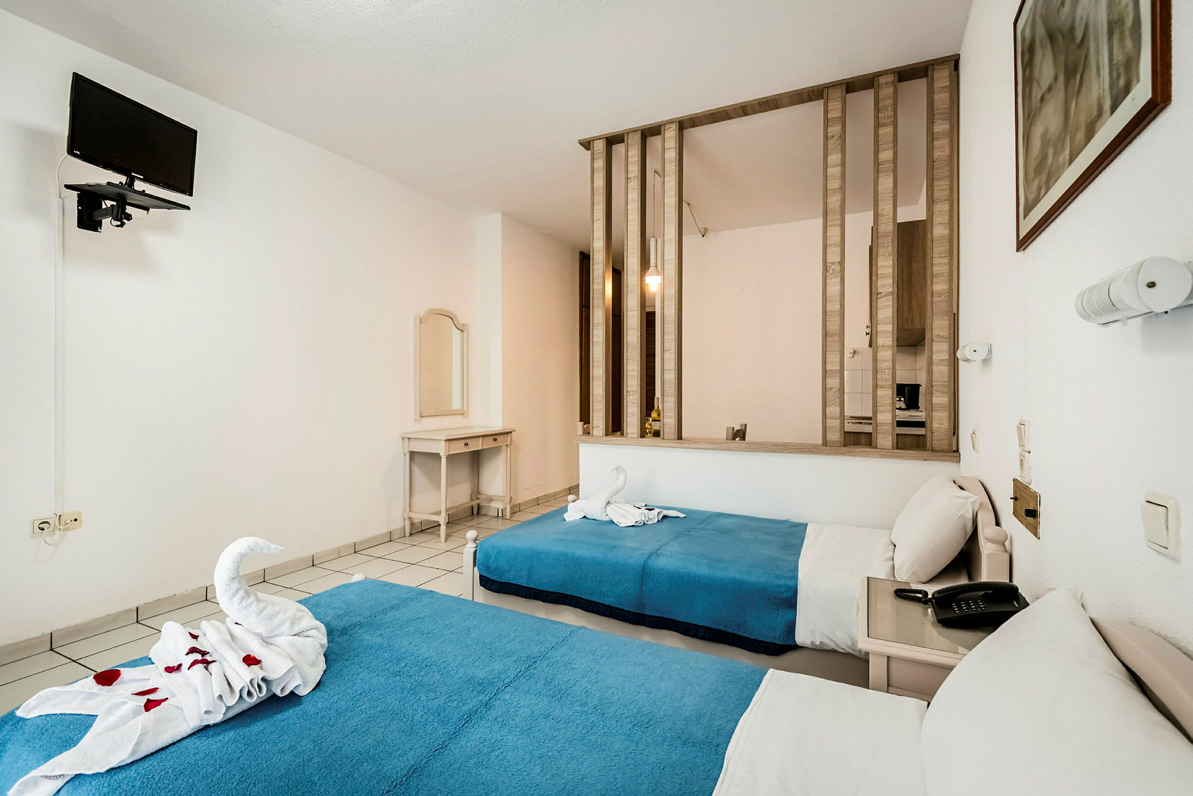 Hotellihuone, jossa on kaksi yksittäistä sänkyä, sininen päiväpeite ja seinälle kiinnitetty televisio. (Tekoälyn luoma teksti)