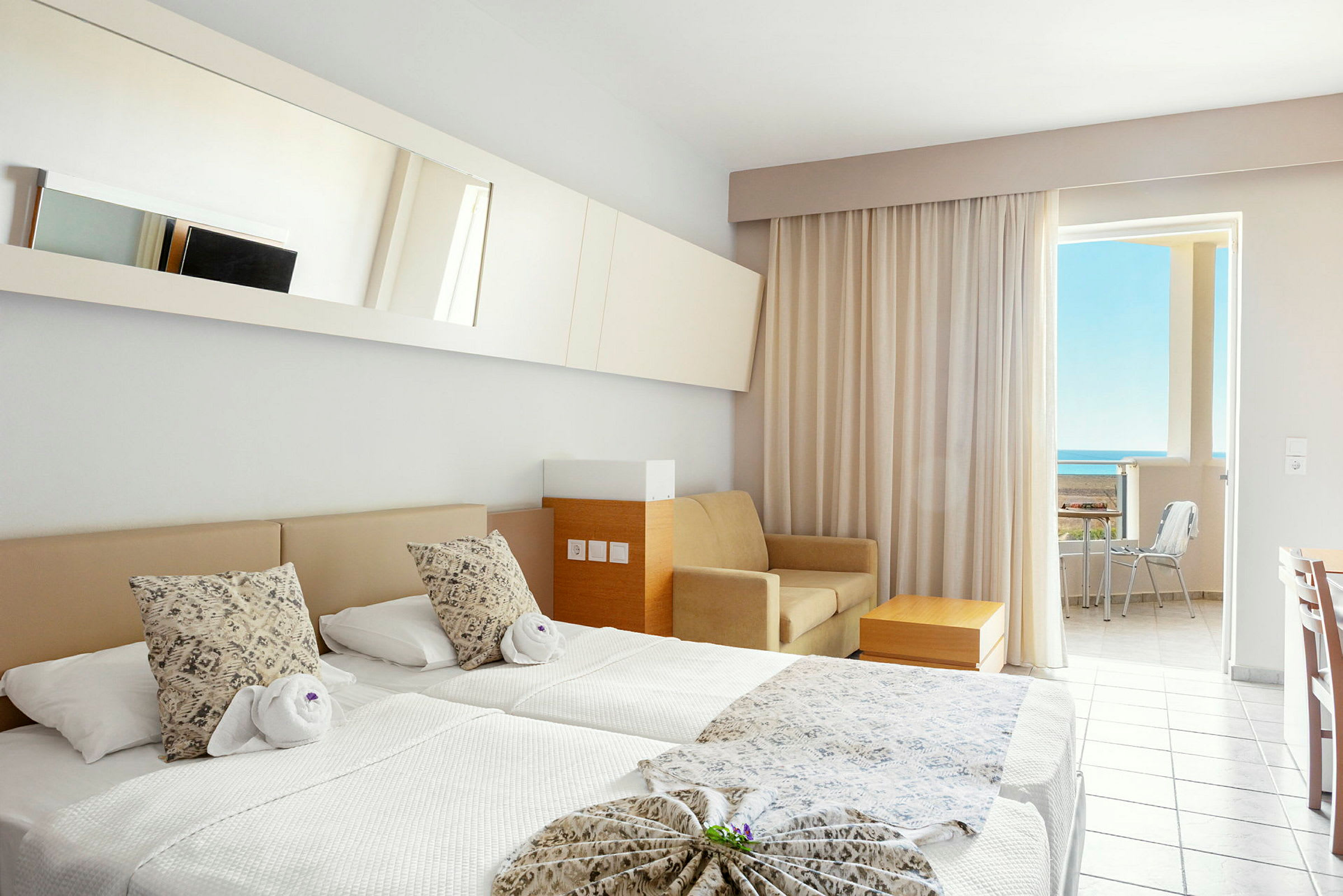 Hotellihuone, jossa kaksi erillistä vuodetta, sohva, pöytä ja parveke merinäkymillä. (Tekoälyn luoma teksti)