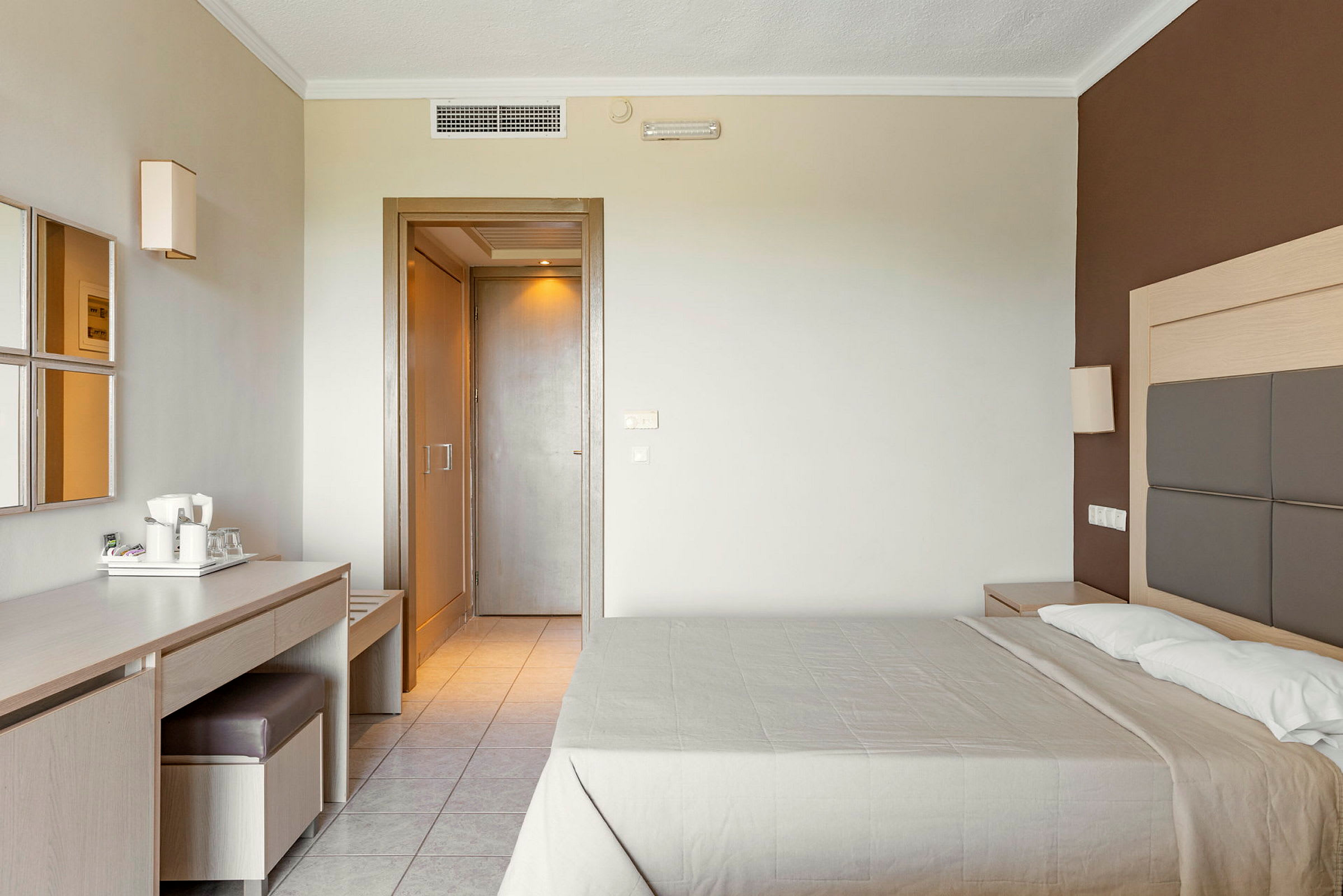 Hotellihuone, jossa on parivuode, kirjoituspöytä tuolin ja peilin kanssa sekä ovi muihin tiloihin. (Tekoälyn luoma teksti)