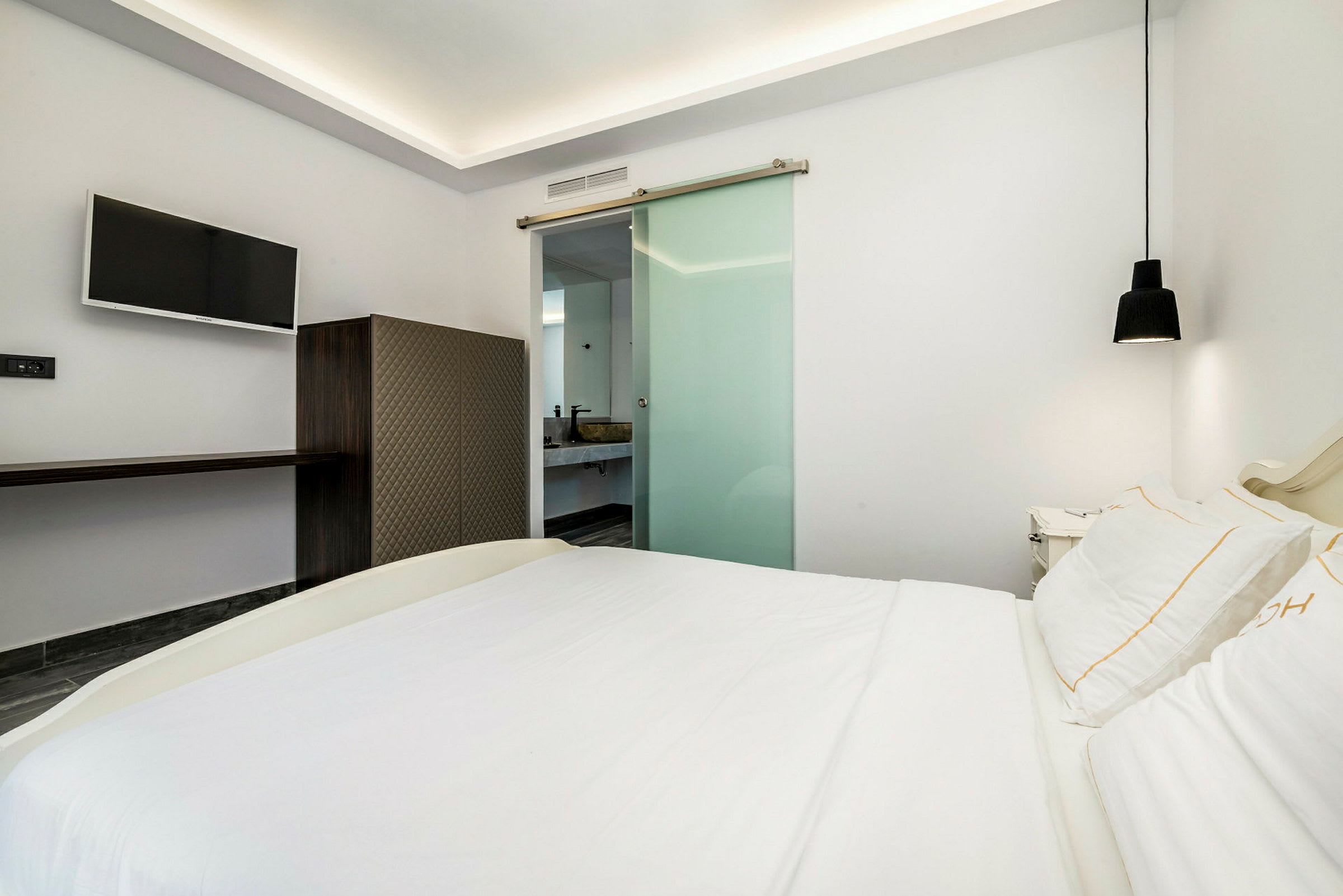 Moderni hotellihuone, jossa on parivuode, seinällä litteänäyttötelevisio ja lasiovi kylpyhuoneeseen. (Tekoälyn luoma teksti)