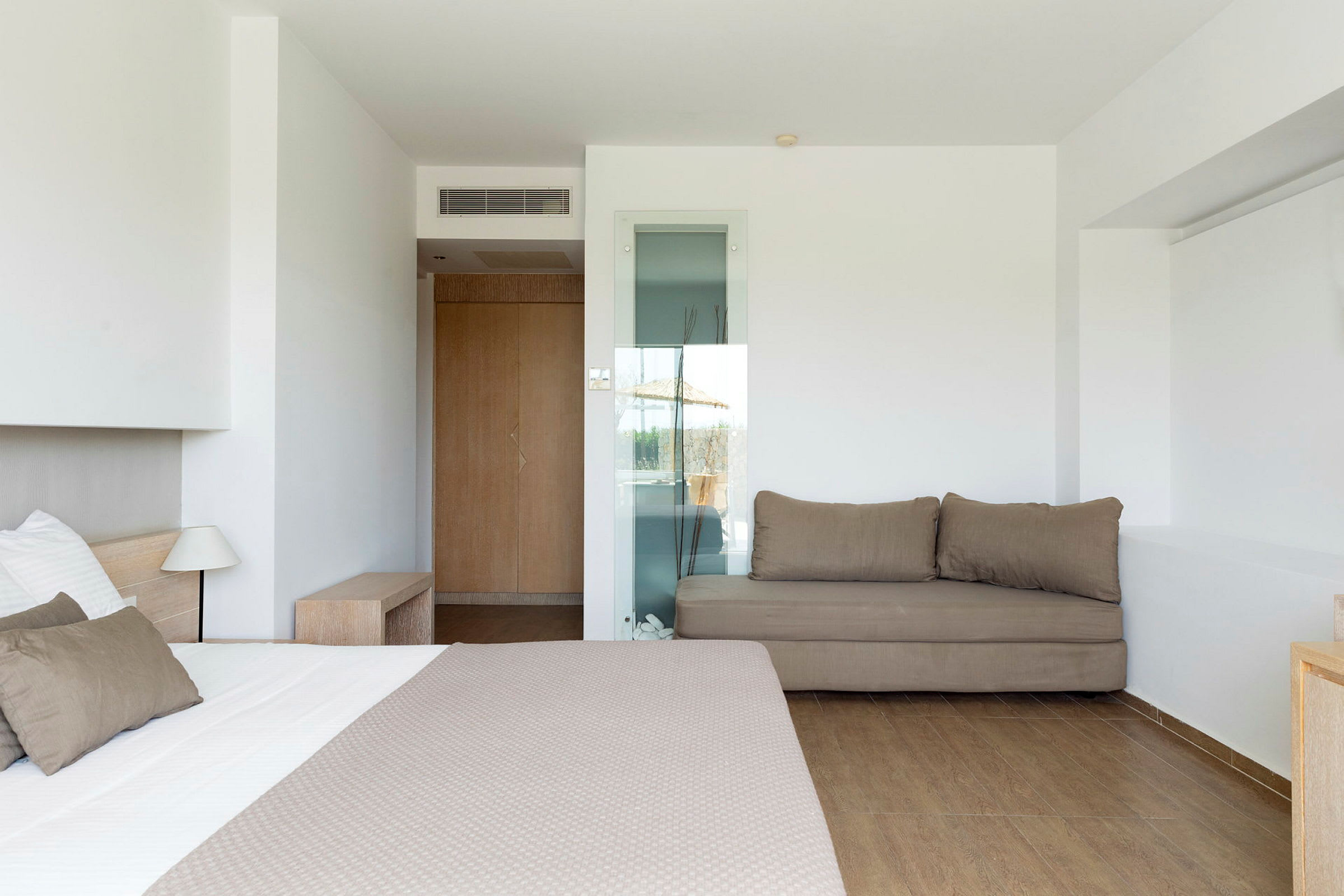 Hotellihuone, jossa sänky, sohva ja vaaleat seinät. (Tekoälyn luoma teksti)