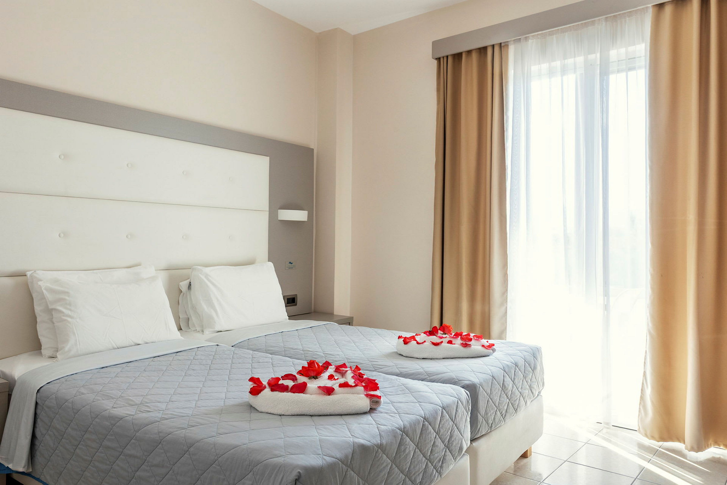 Hotellihuone, jossa on kaksi yhden hengen vuodetta koristeltu punaisilla ruusun terälehdillä. (Tekoälyn luoma teksti)