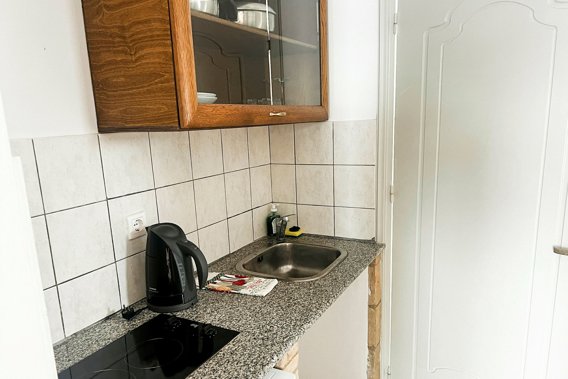 Pieni keittiö, jossa on tiskiallas, induktioliesi, vedenkeitin ja kaappi. (Tekoälyn luoma teksti)