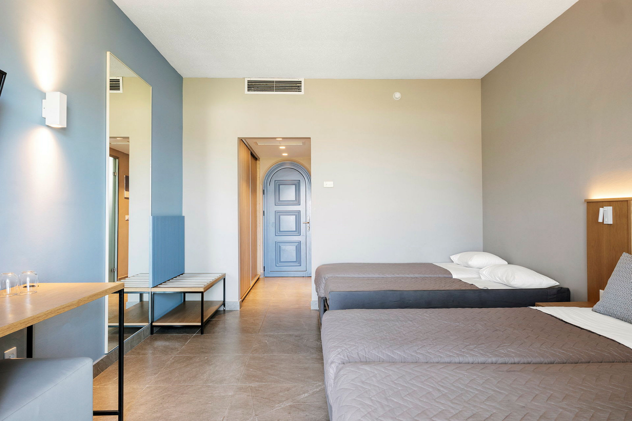Hotellihuone, jossa on kaksi yhden hengen vuodetta, kirjoituspöytä ja sininen ovi. (Tekoälyn luoma teksti)