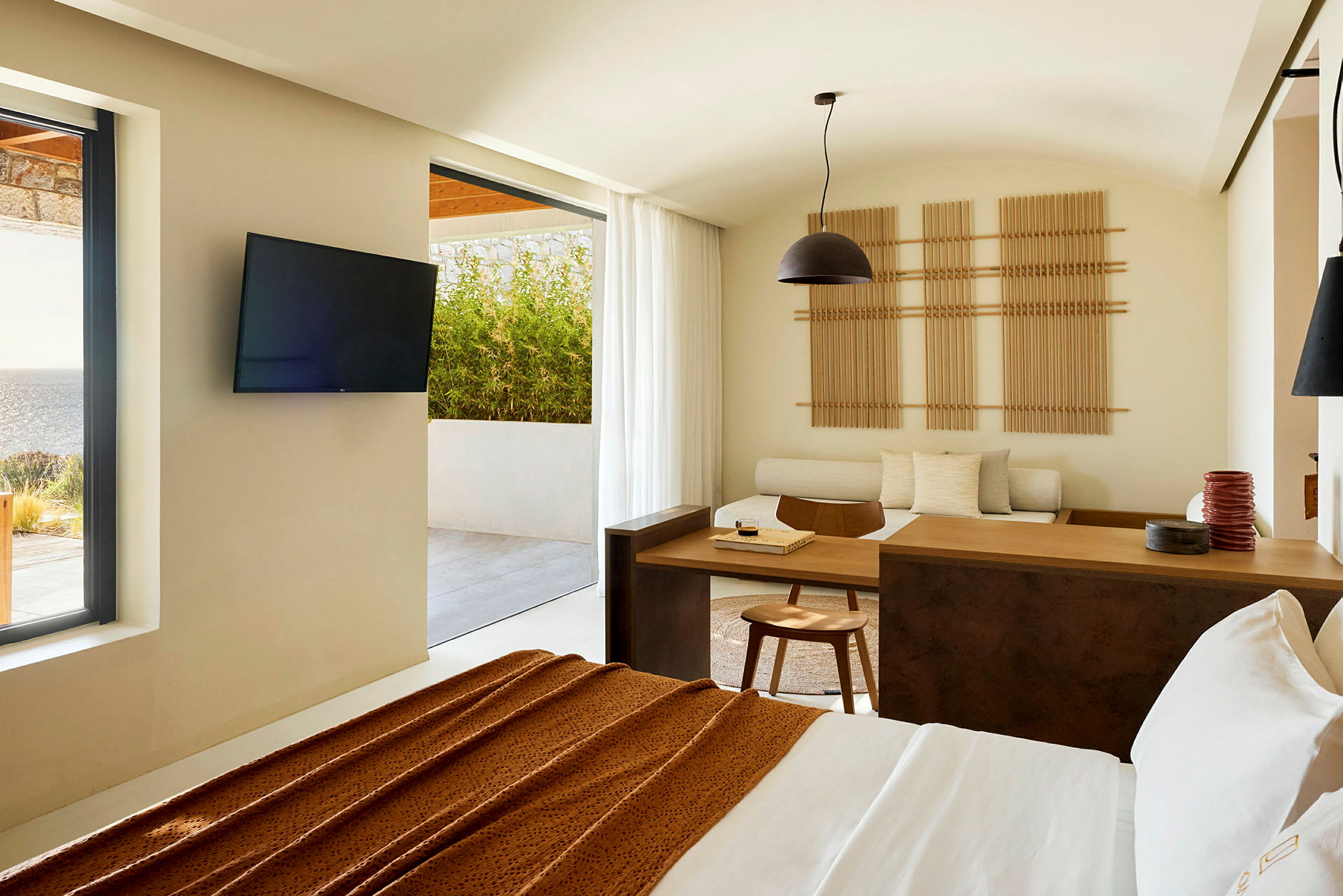 Moderni hotellihuone, josta on näkymä terassille ja merelle, sisustettu minimalistisilla huonekaluilla ja vaaleilla väreillä. (Tekoälyn luoma teksti)