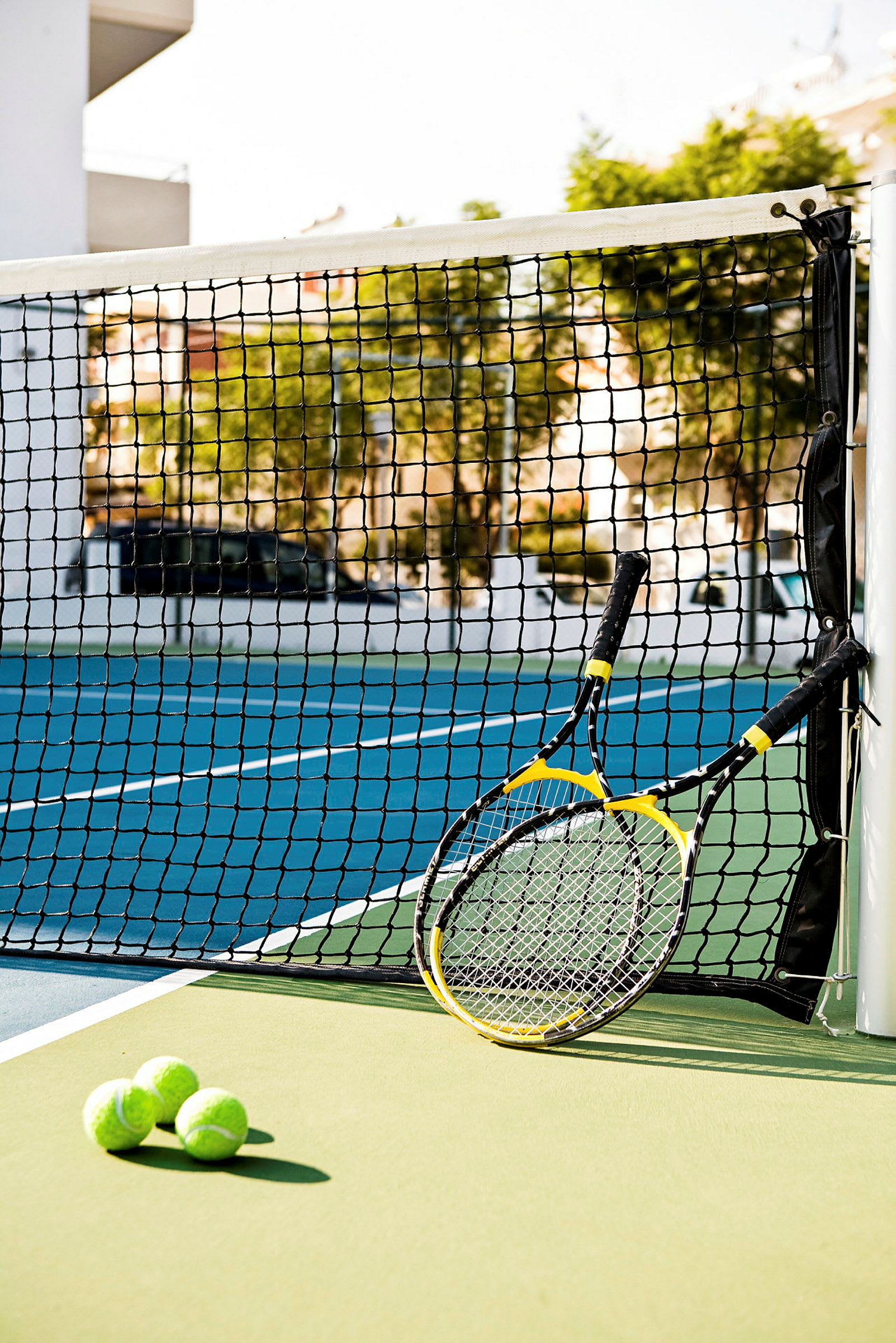 Kaksi tennismailaa ja kolme tennispalloa verkon vieressä tenniskentällä. (Tekoälyn luoma teksti)