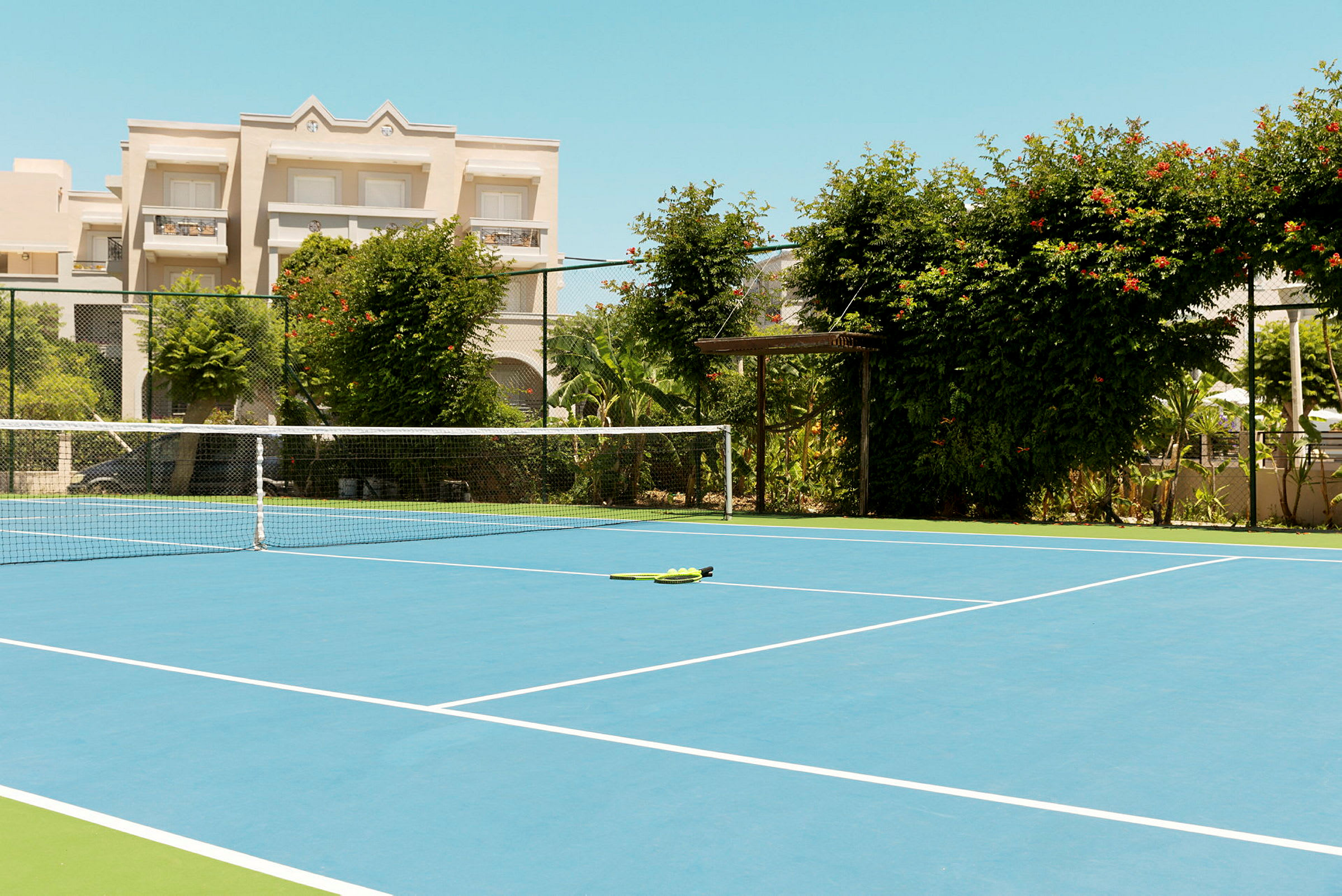 Tenniskenttä, jossa verkko ja vihreää kasvillisuutta ympärillä. (Tekoälyn luoma teksti)