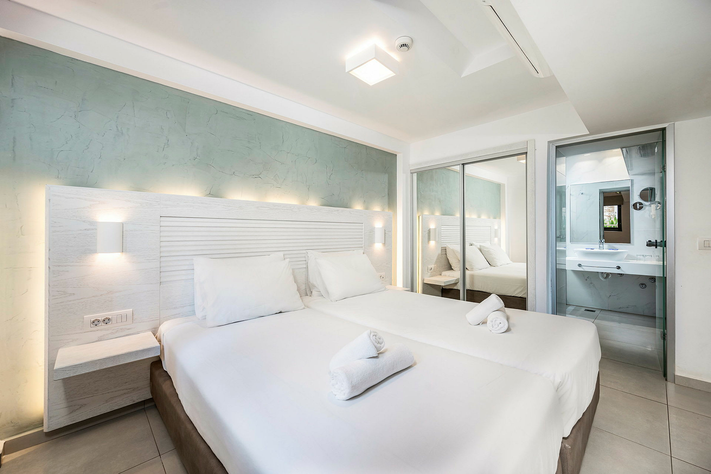 Hotellihuone, jossa parivuode, valkoiset vuodevaatteet ja taustalla näkyvä kylpyhuone. (Tekoälyn luoma teksti)