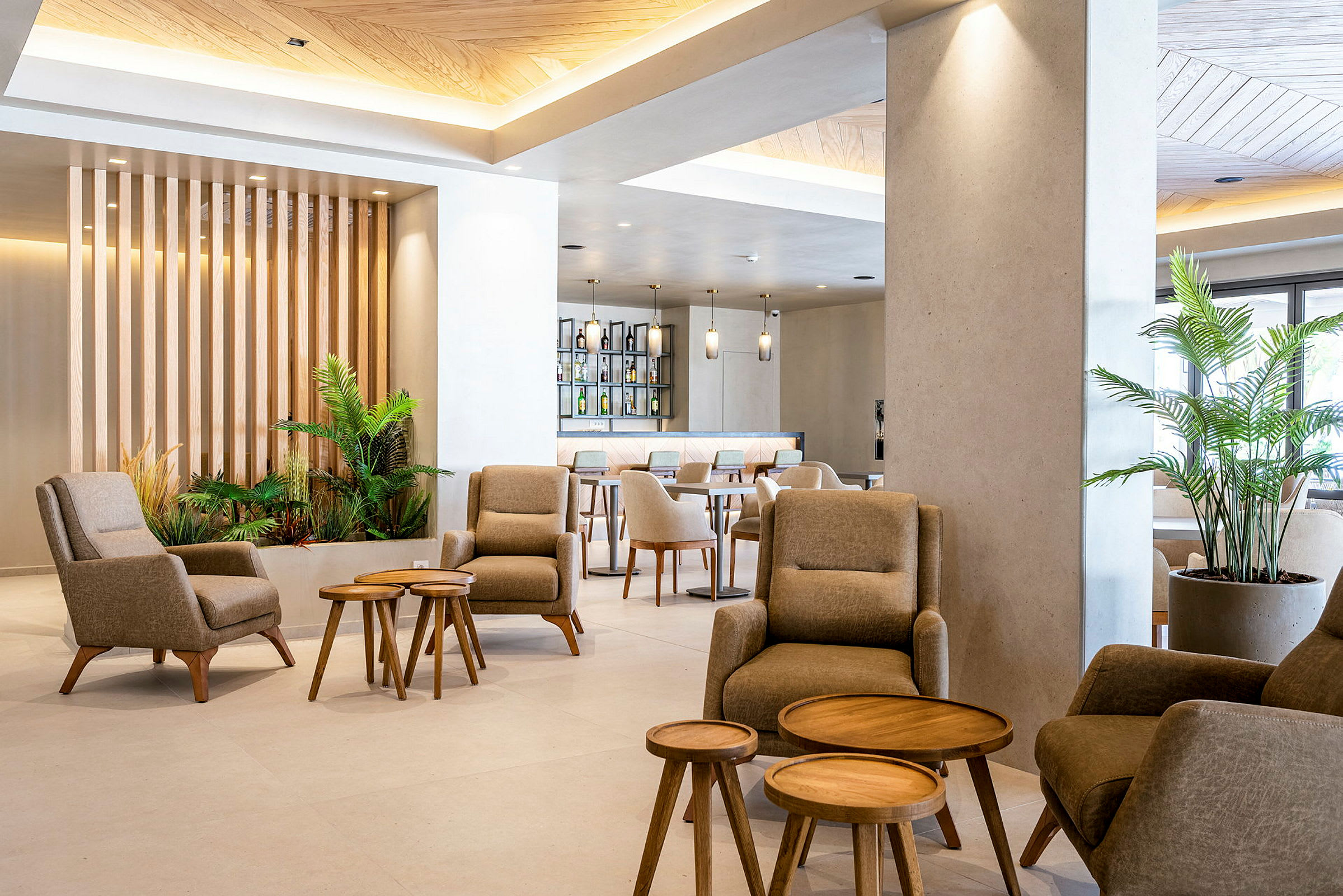 Moderni lounge-alue, jossa mukavia tuoleja ja pieniä puupöytiä, ympäröitynä istutetuilla kasveilla. (Tekoälyn luoma teksti)