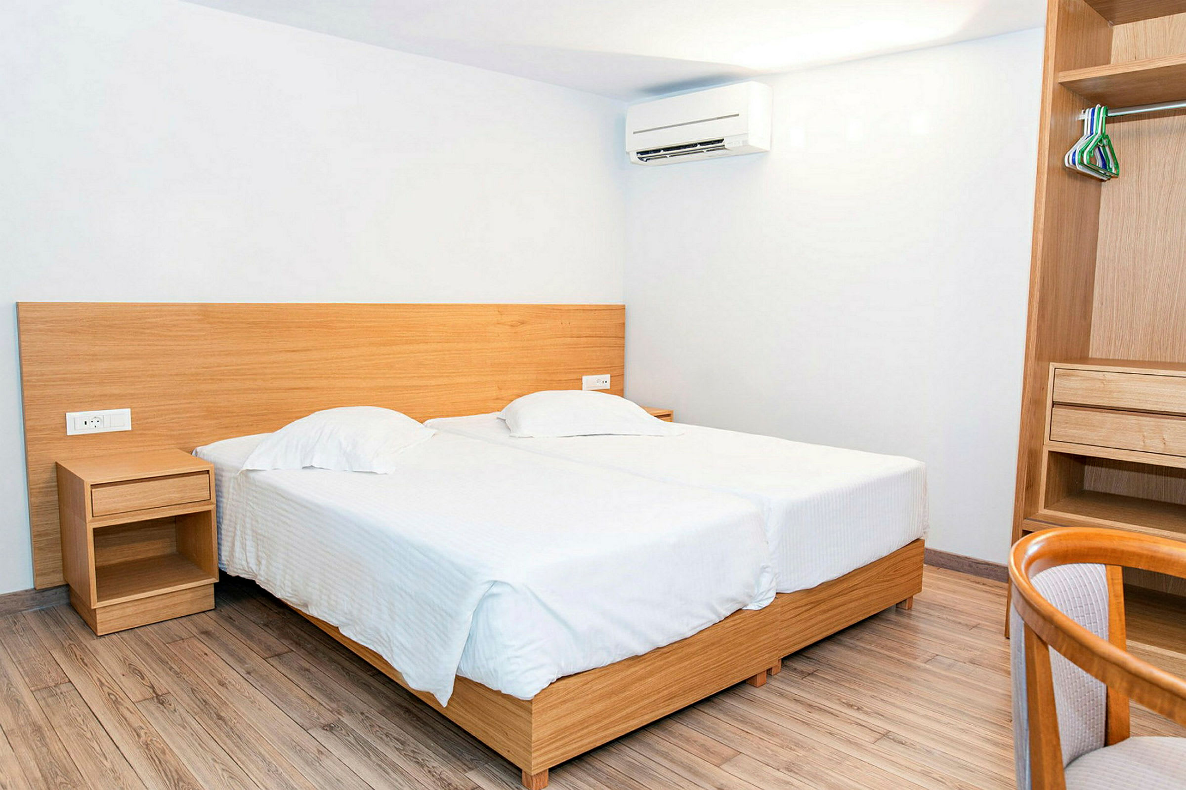 Hotellihuoneen sisustus, jossa on kaksi erillistä vuodetta ja avoin vaatekaappi. (Tekoälyn luoma teksti)