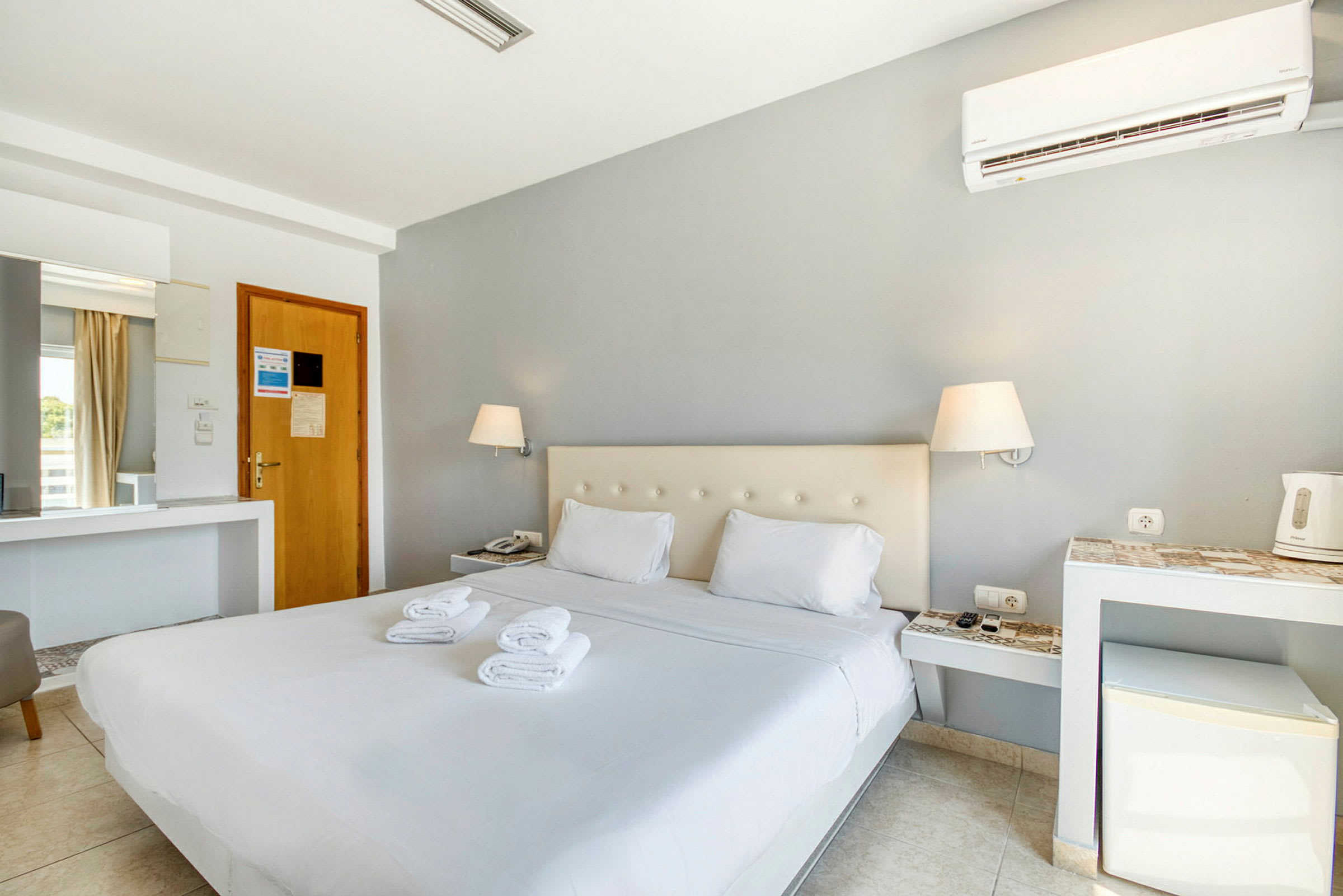 Hotellihuone, jossa on parivuode, kaksi lamppua ja pieni minijääkaappi. (Tekoälyn luoma teksti)