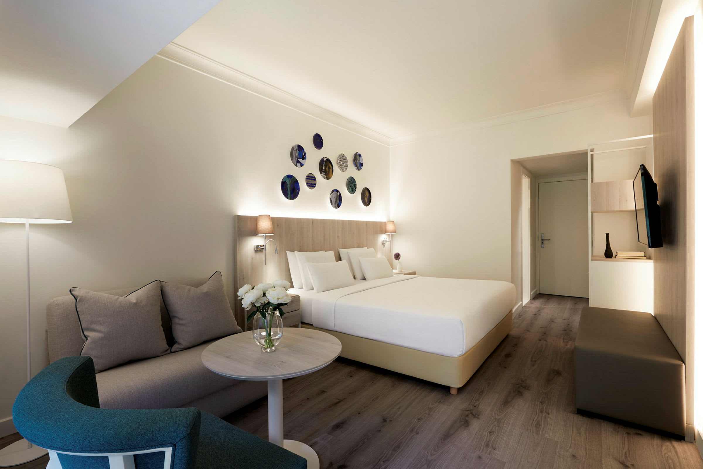 Hotellihuone, jossa on sänky, sohva ja sohvapöytä, koristeena moderneja yksityiskohtia. (Tekoälyn luoma teksti)