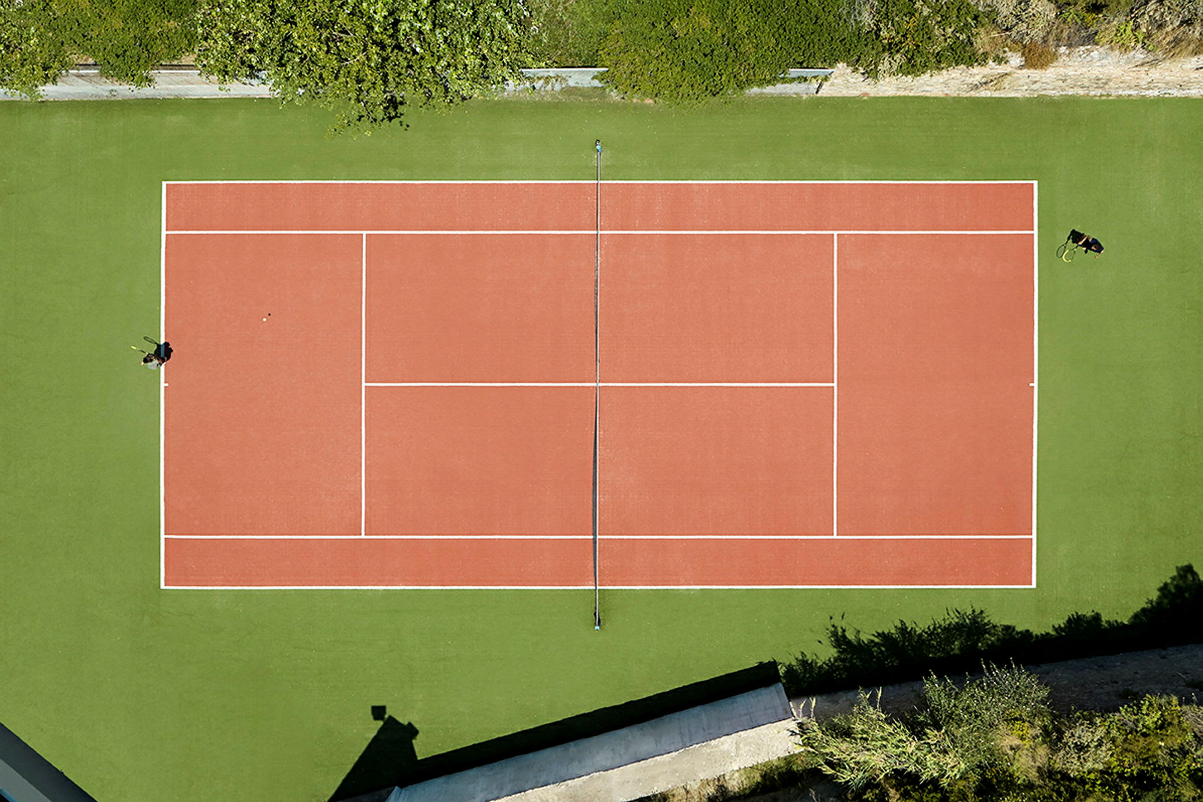 Tenniskenttä kuvattuna ylhäältä, ympärillä vihreää. (Tekoälyn luoma teksti)