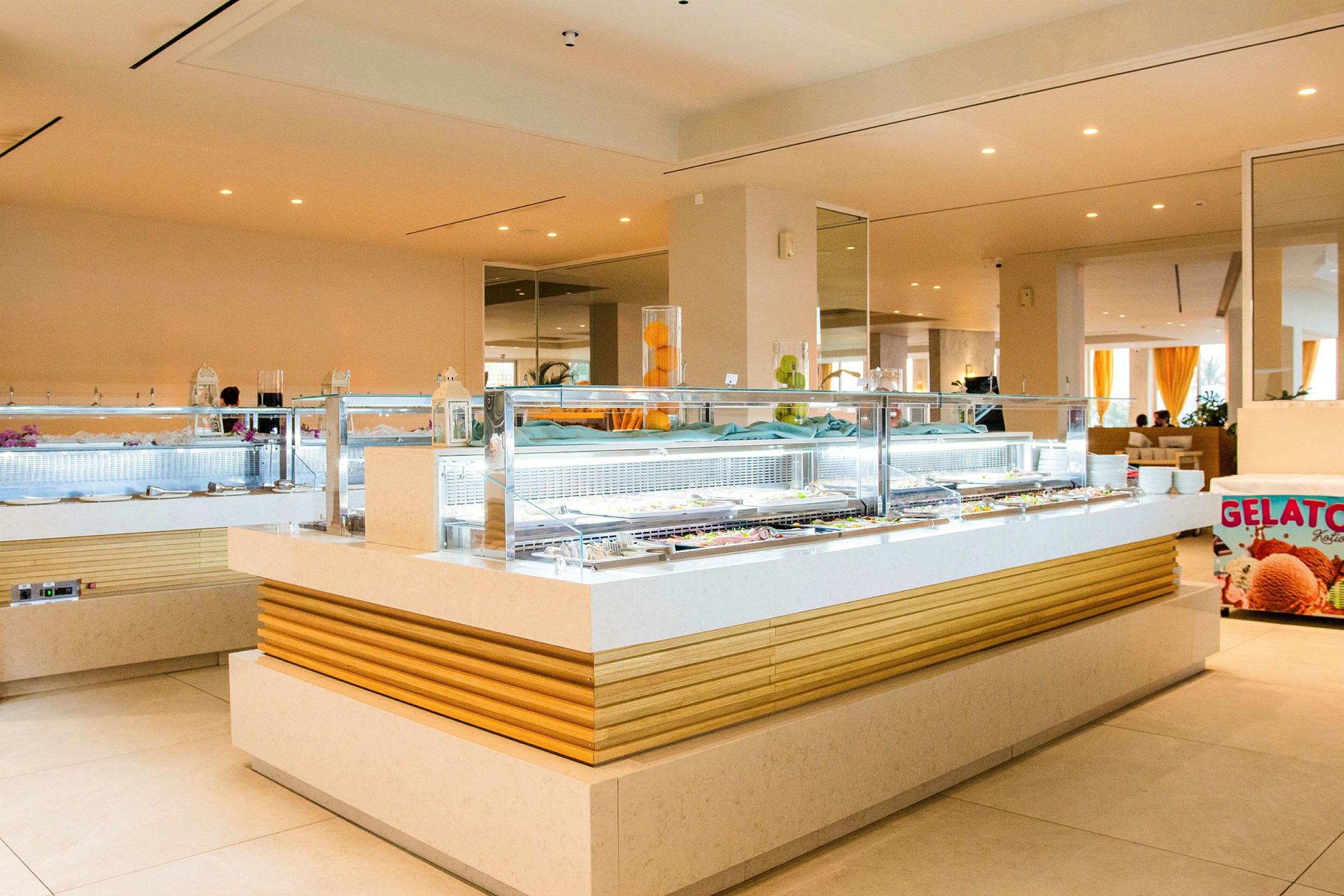 Kuva modernista buffetista, jossa on "Gelato"-jäätelökyltti ja lasipinta erilaisilla ruokavaihtoehdoilla. (Tekoälyn luoma teksti)