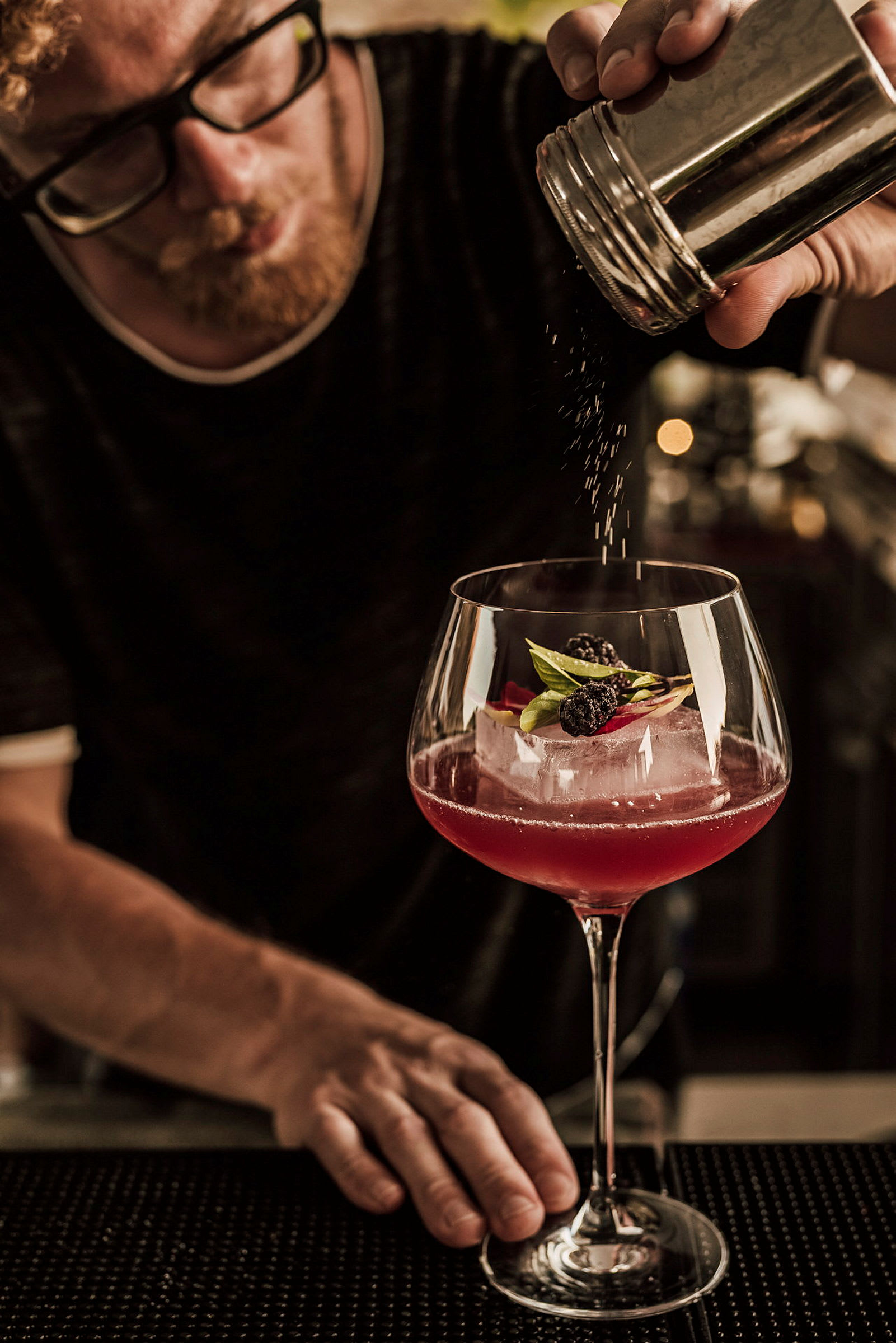 Käsi ripottelee jauhetta cocktailin päälle, joka on koristeltu marjoilla ja lehdillä. (Tekoälyn luoma teksti)