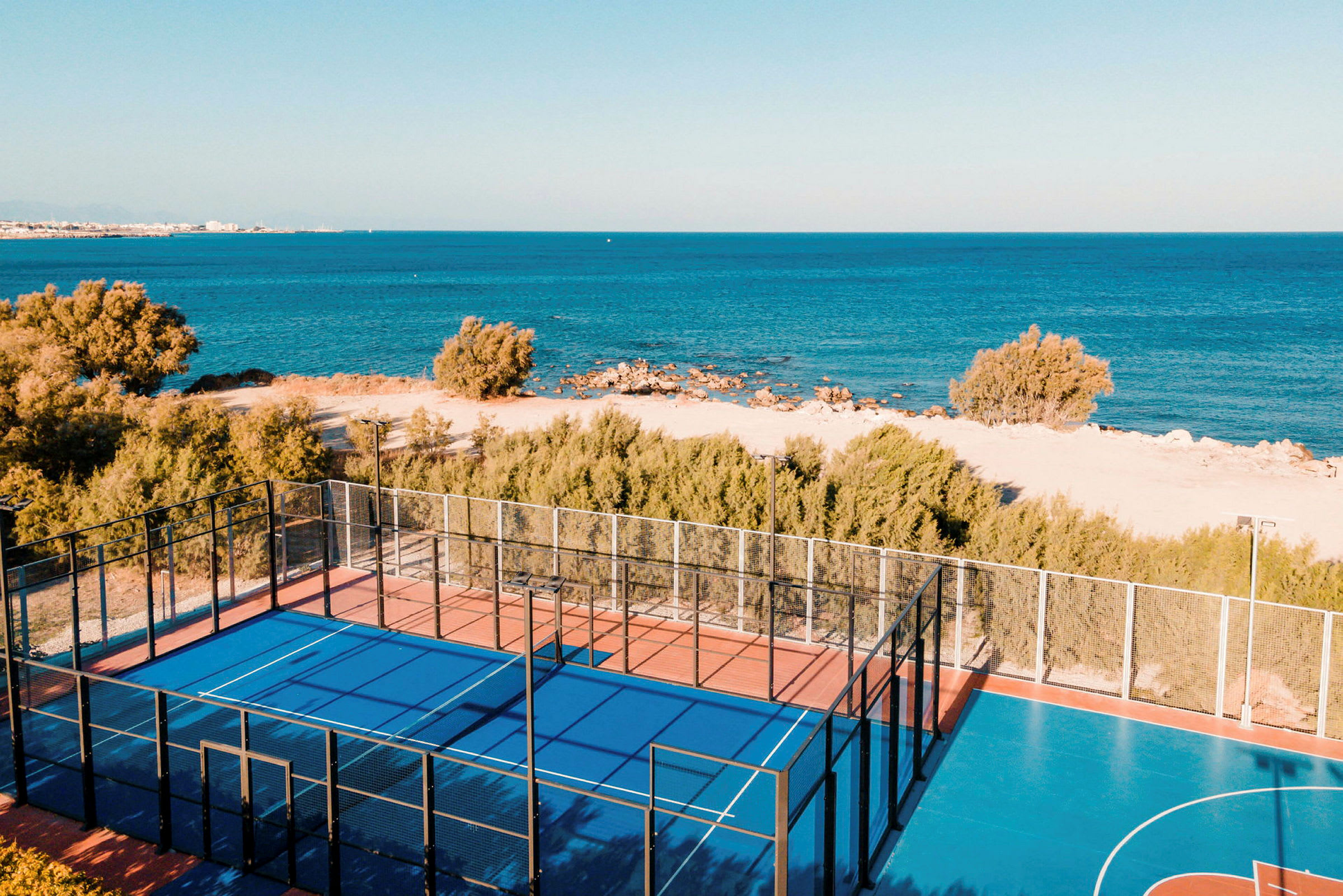 Sinipohjainen padelkenttä lähellä rantaa ja merta. (Tekoälyn luoma teksti)