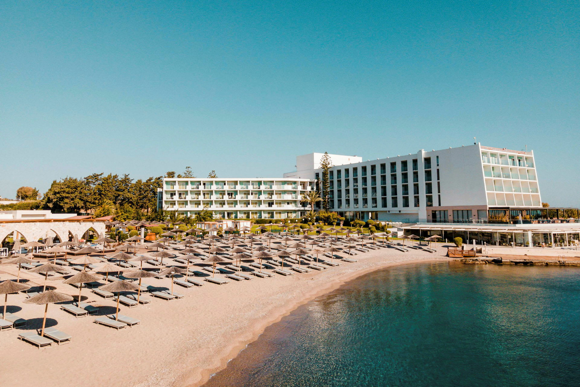 Näkymä hotellista ja rannasta, jossa on aurinkotuoleja ja varjoja. (Tekoälyn luoma teksti)