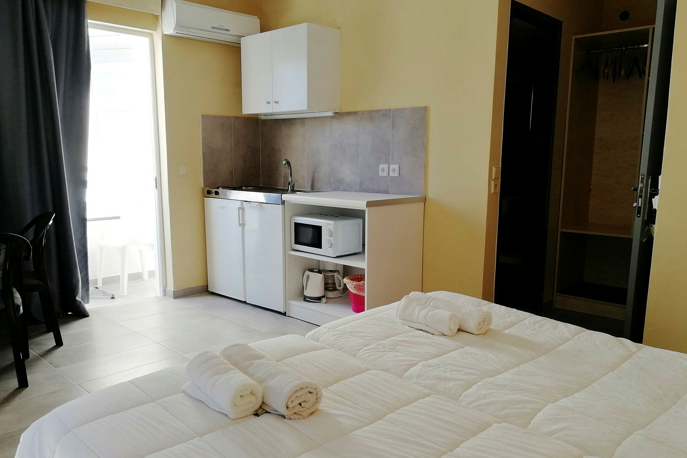 Hotellihuone, jossa pieni keittiötila, sänky, jolla on pyyhkeitä, ja kaappi. (Tekoälyn luoma teksti)