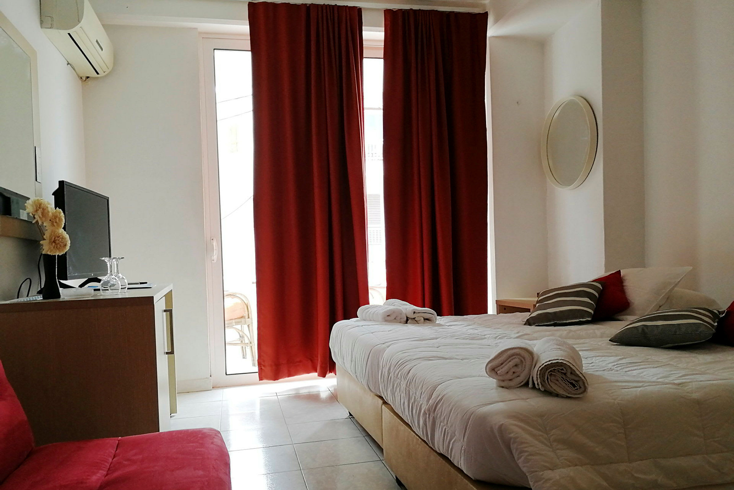 Hotellihuone, jossa on parisänky, punaiset verhot ja televisio lipaston päällä. (Tekoälyn luoma teksti)