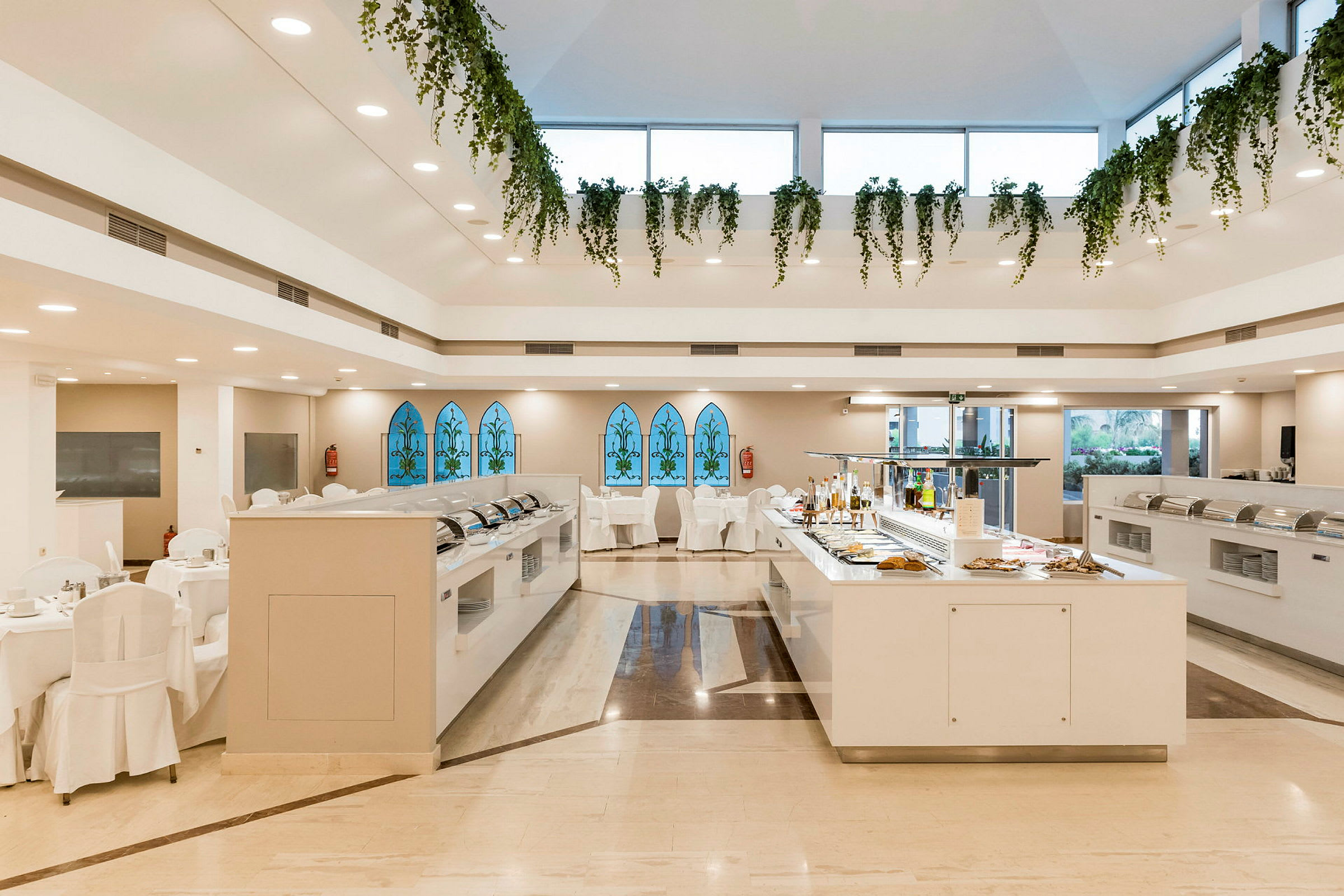 Näkymä buffet-ravintolasta, jossa riippuvia viherkasveja ja suuria lasi-ikkunoita. (Tekoälyn luoma teksti)